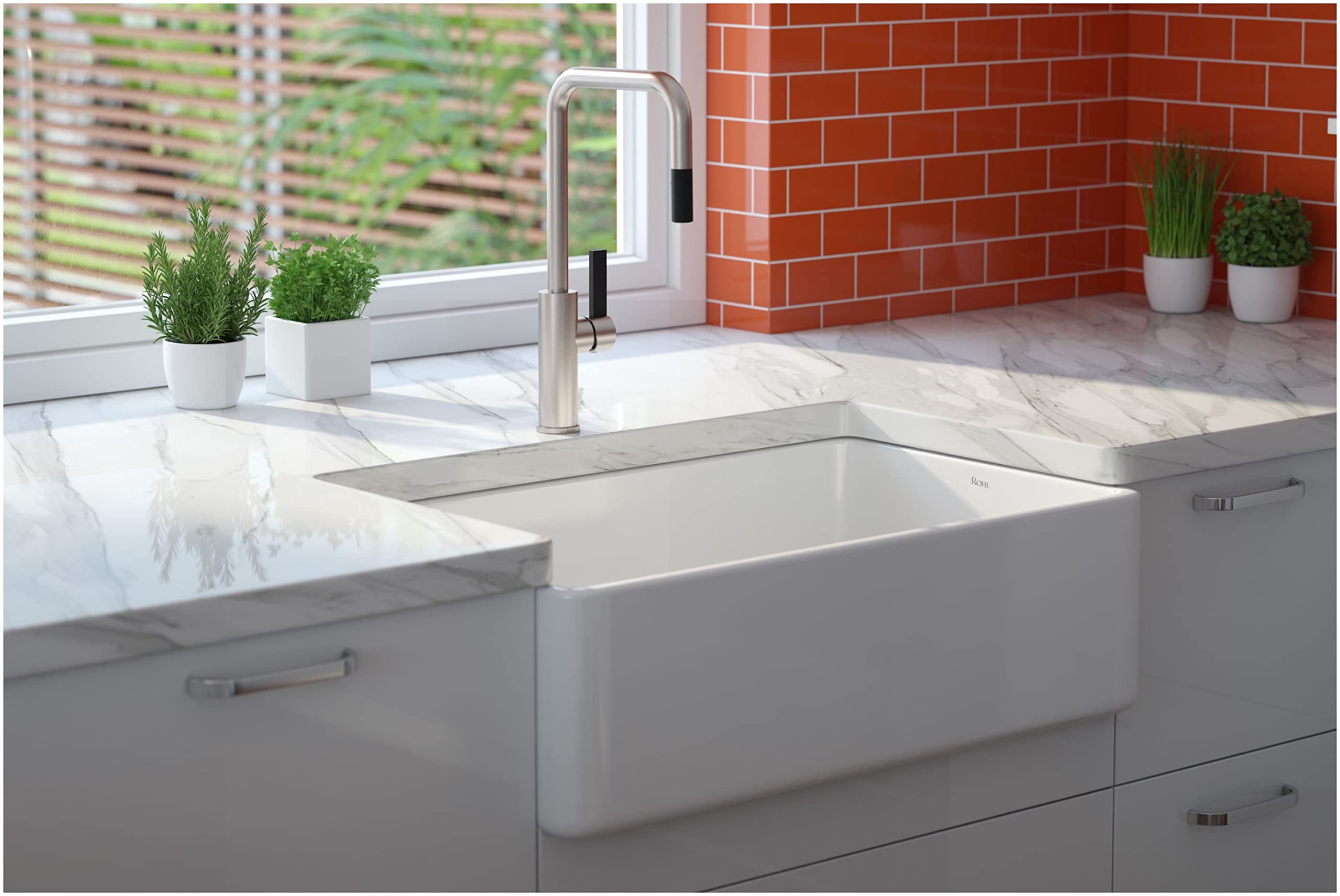Polished chrome pull-down kitchen faucet with U-shaped spout mounted above white farmhouse sink on marble countertop.