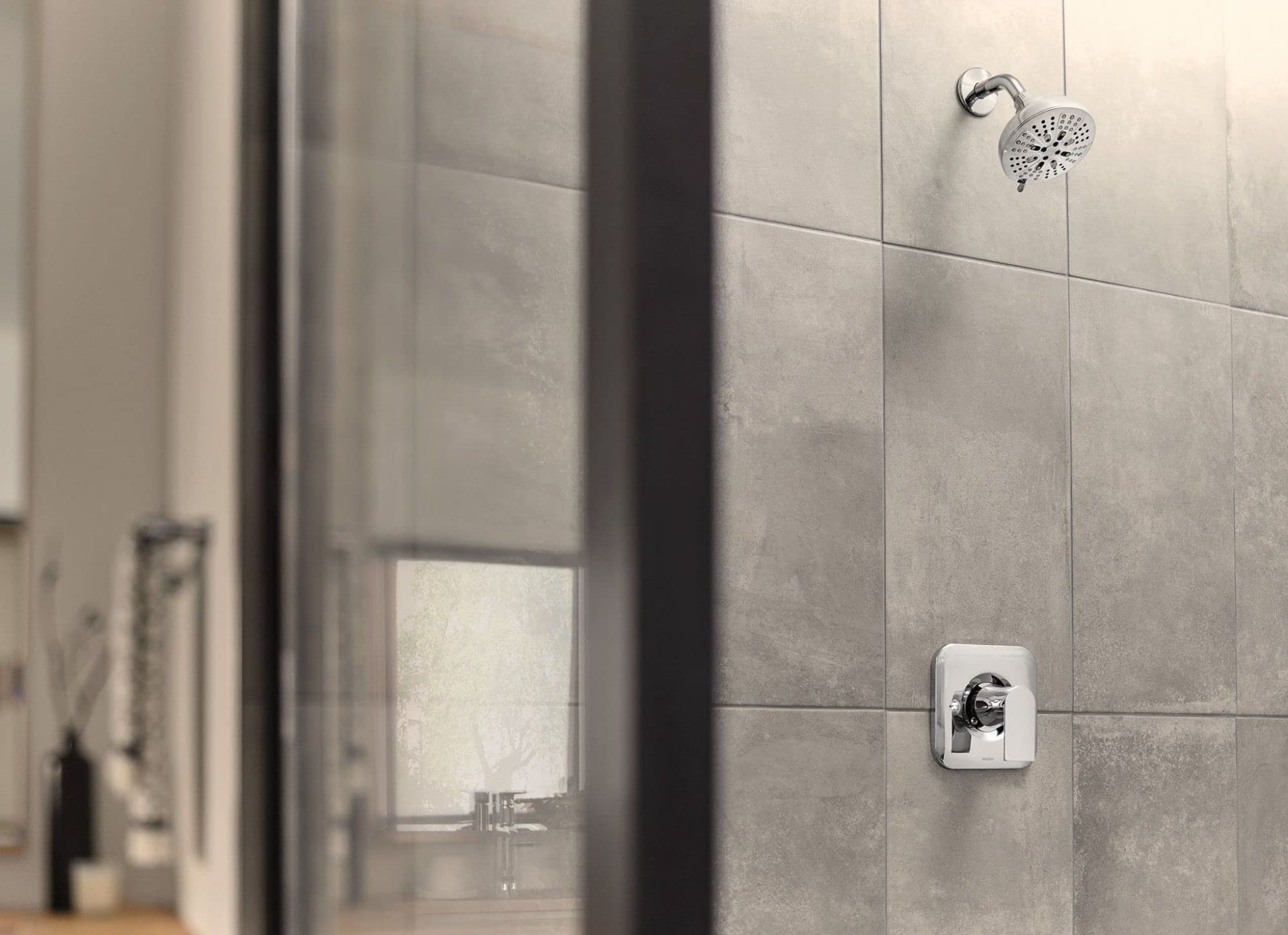 Chrome single-handle shower valve trim with round showerhead mounted on tiled bathroom wall.