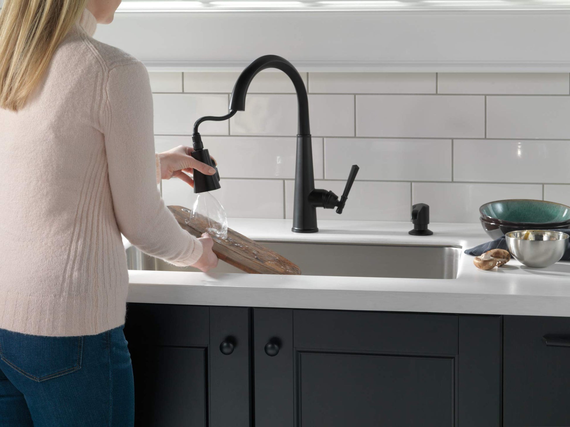 Matte black metal soap dispenser mounted beside kitchen sink faucet on countertop.