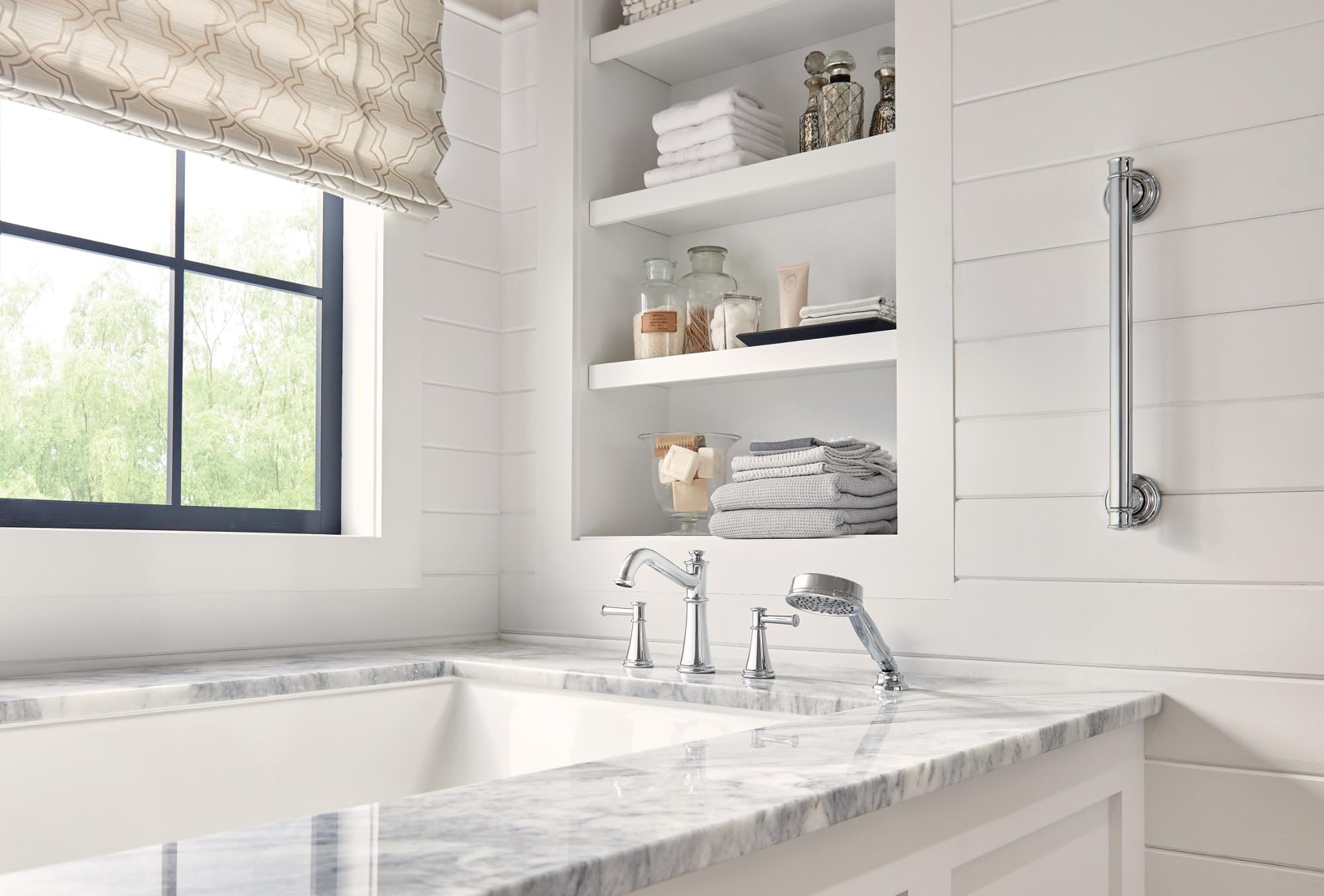 Polished nickel Roman tub faucet with dual handles, spout, and handheld showerhead mounted on marble deck.