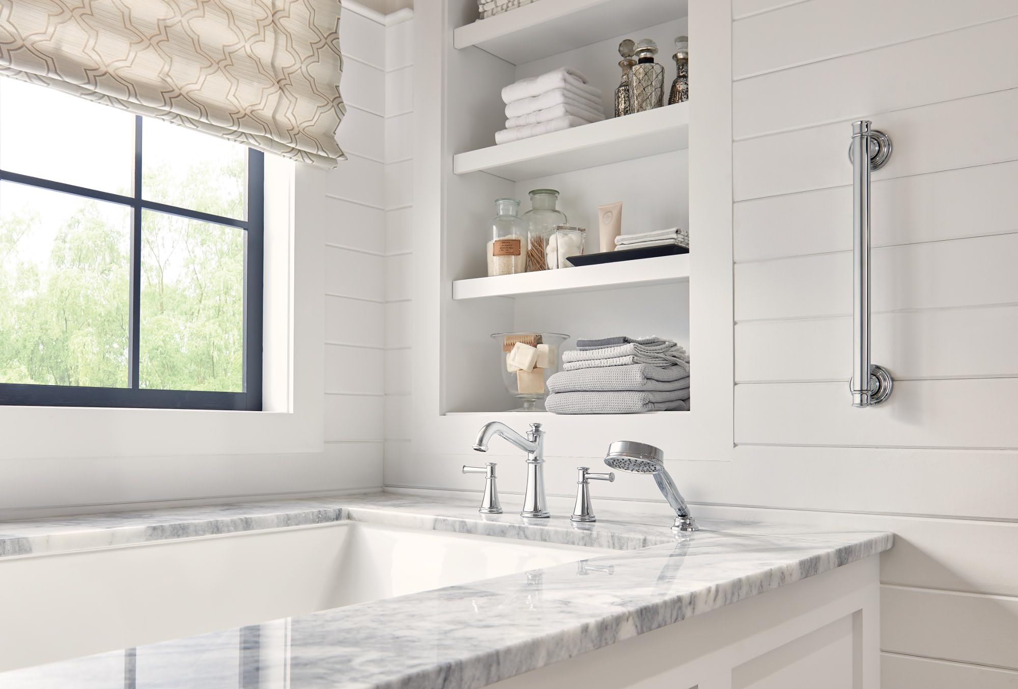Polished nickel Roman tub faucet with dual handles, spout, and handheld showerhead mounted on marble deck.