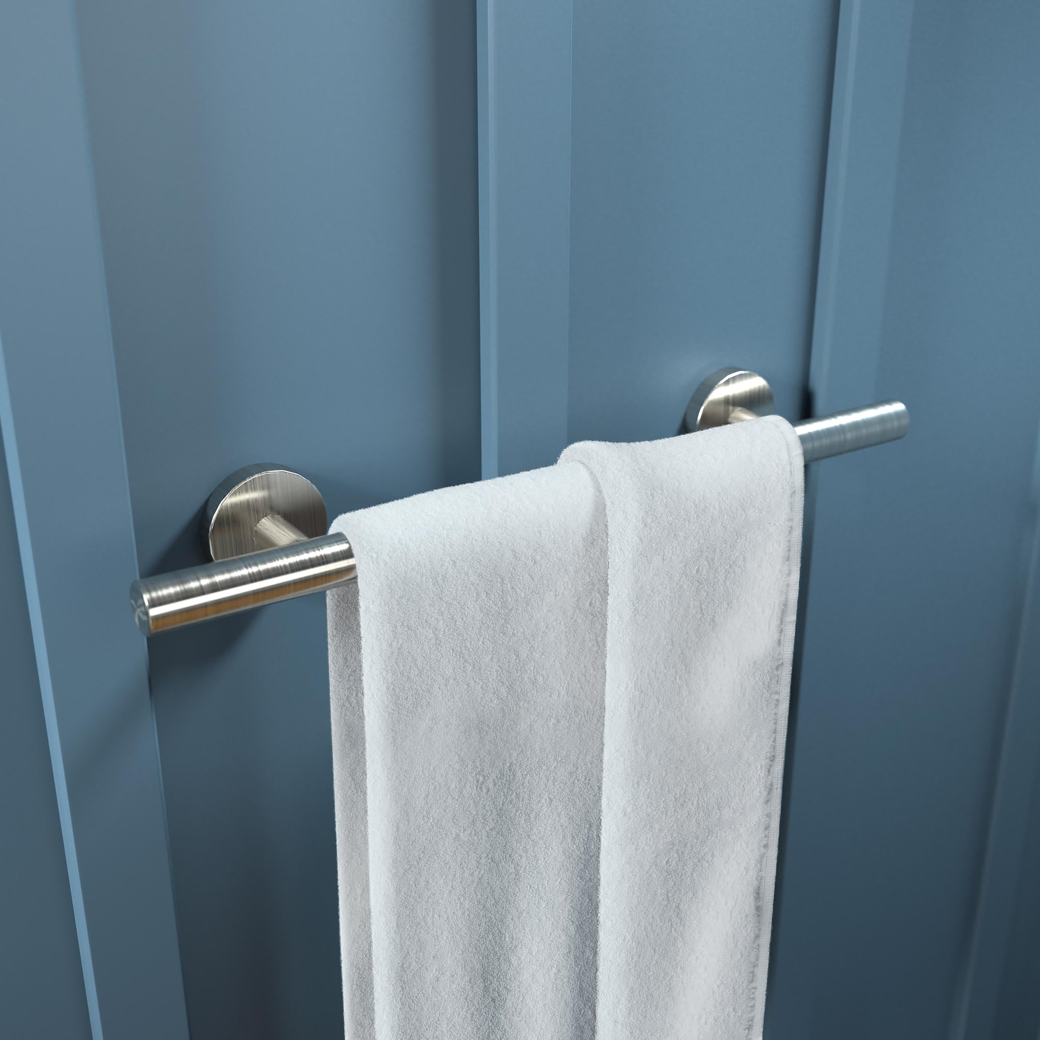 Brushed nickel towel bar mounted on blue wall with white towel draped over cylindrical rod.