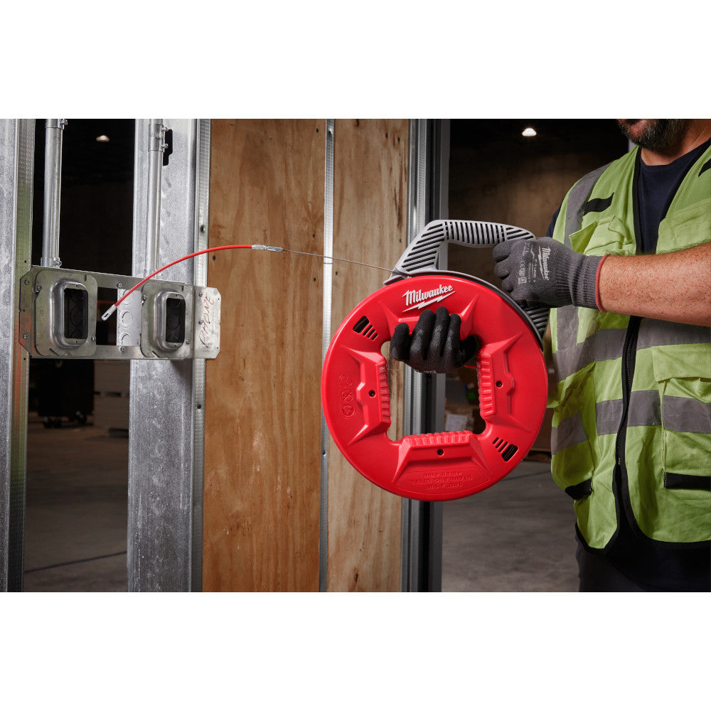 Milwaukee fish tape reel with red spool and stainless steel cable being used in electrical conduit installation.