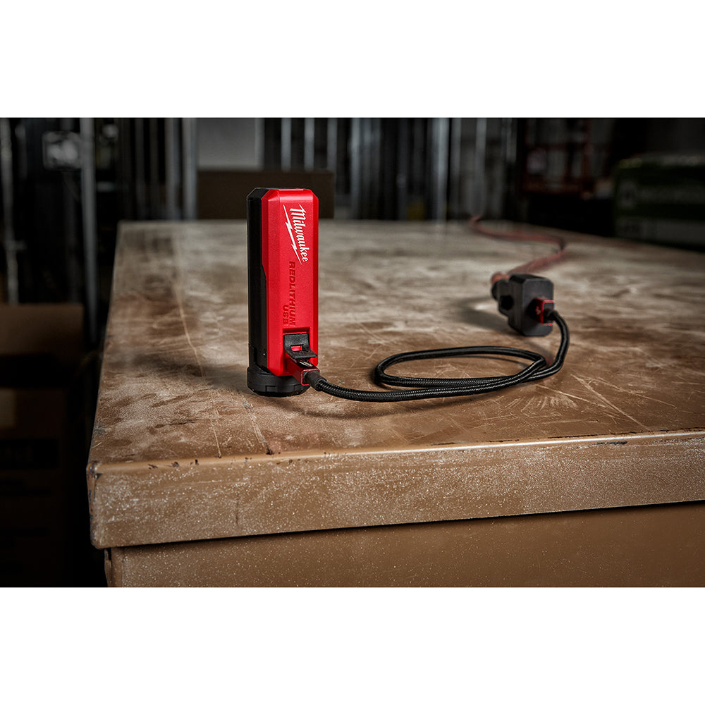 Red and black Milwaukee REDLITHIUM USB charger with attached power cable on wooden work surface.