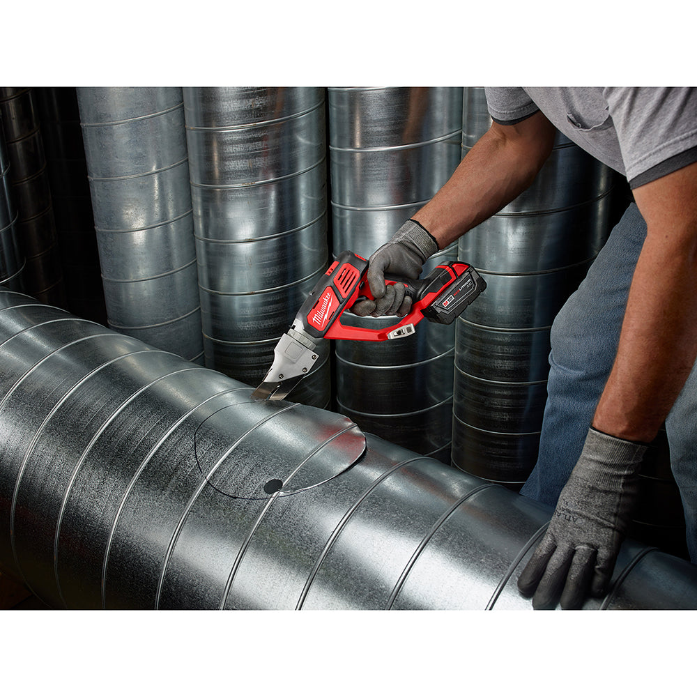 Red and black cordless shear with battery cutting through metal ductwork in an industrial setting.