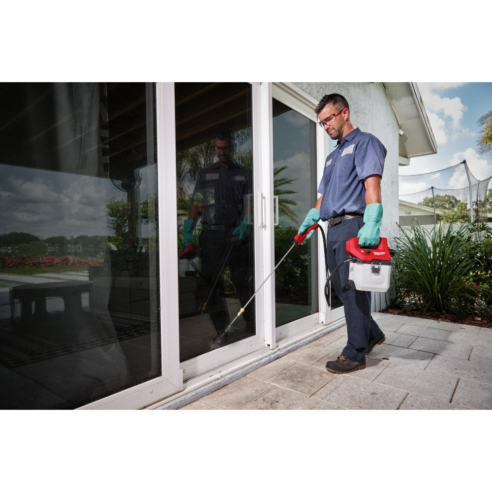 Man in blue shirt and gloves holding a red and white handheld sprayer tank with wand attachment.