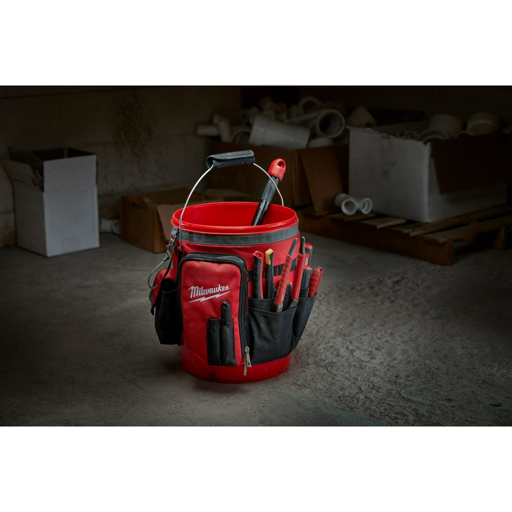 Red and black Milwaukee bucket organizer bag with handles, multiple pockets, and tools inside on concrete floor.