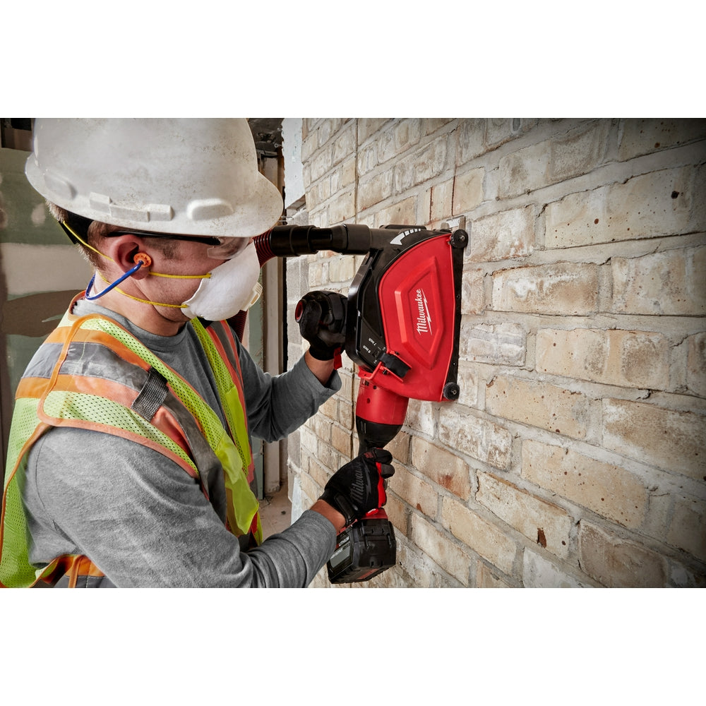 Worker using red Milwaukee angle grinder with cutting shroud attachment against brick wall.