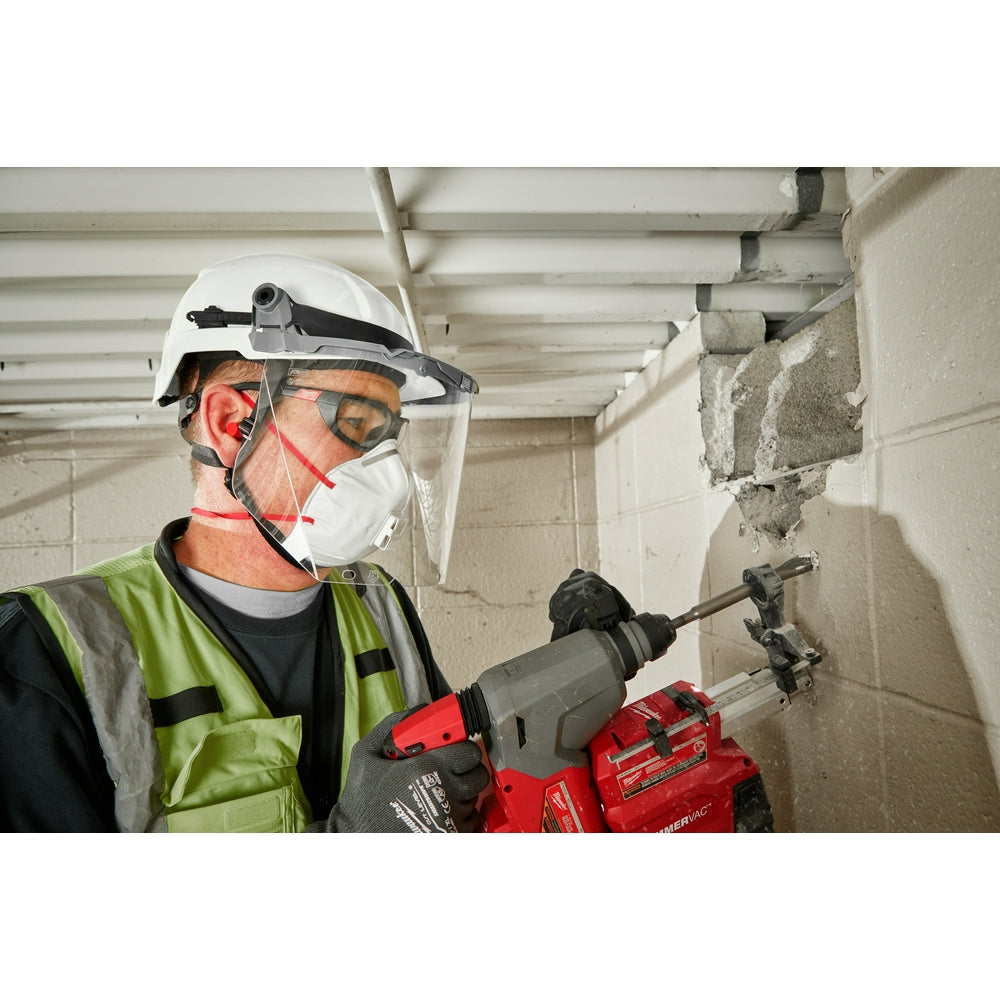 Gray safety helmet with front brim, face shield, and chin strap worn by worker holding power tool.