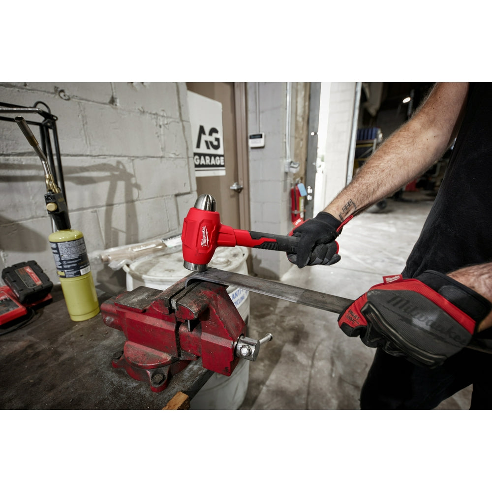 Red and black dead blow hammer with ball peen head held in workshop vise by person wearing work gloves.