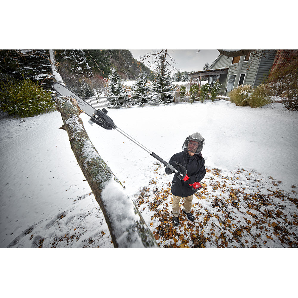 Black Milwaukee pole saw guide bar attached to extended pole saw being used to cut tree branch in snowy yard.
