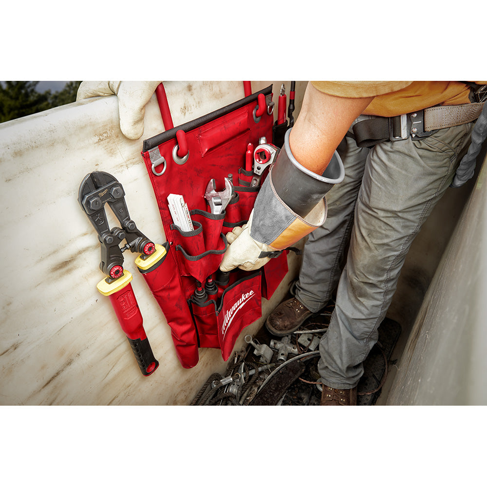 Red tool apron with multiple pockets holding pliers, wrench, and other hand tools, worn by worker on pole.