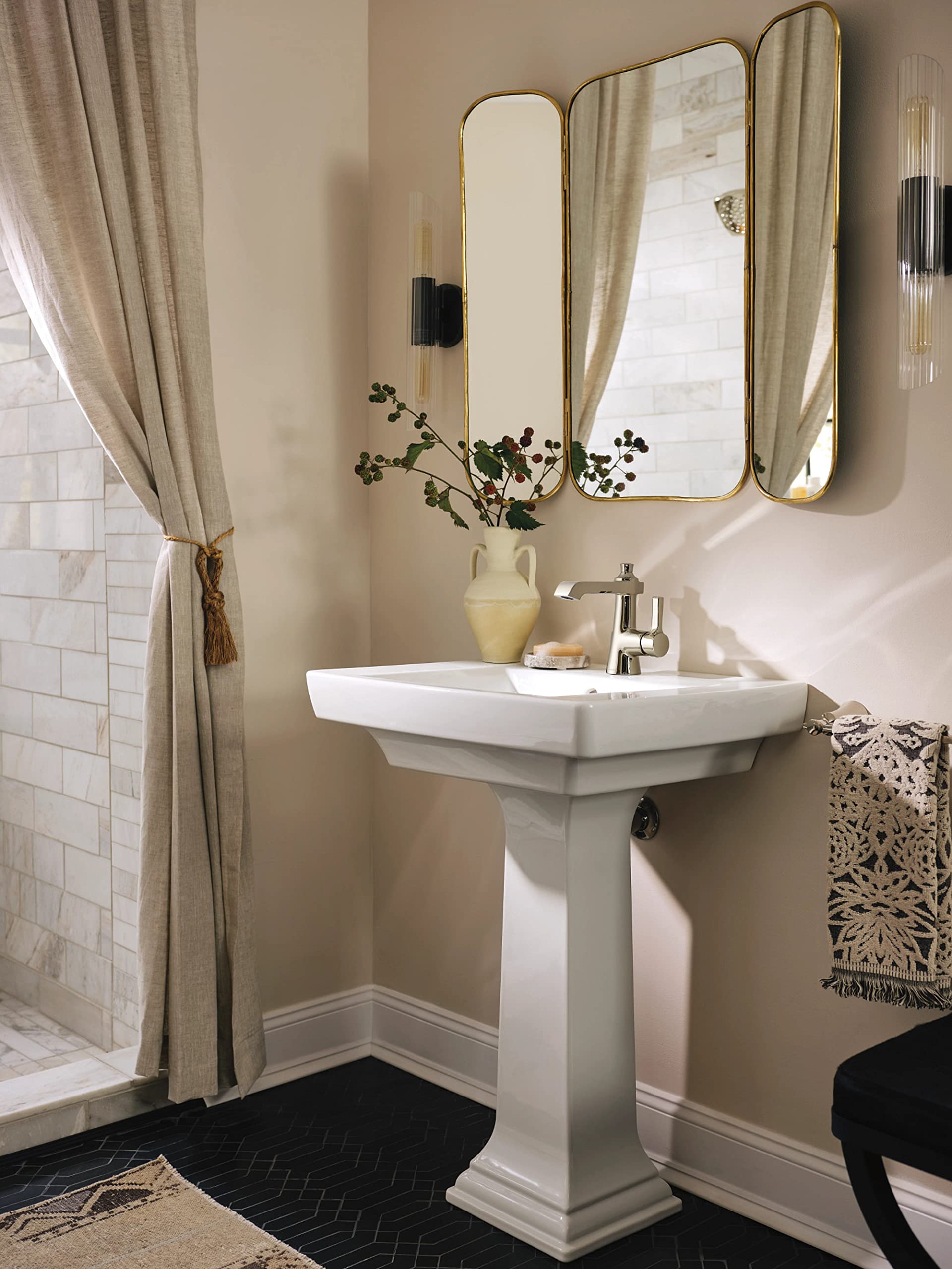 Polished nickel single-handle faucet with curved spout mounted above white pedestal sink.