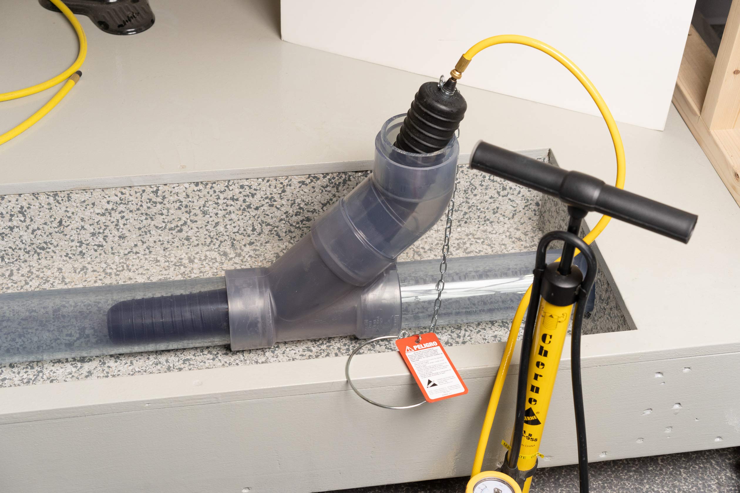 Long test-ball plug with black accordion-style accordion connector and yellow cable attached to metal pipe.