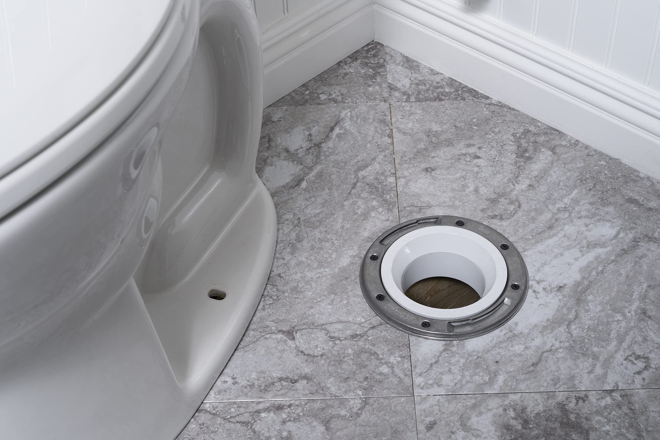 White PVC closet flange with stainless steel ring installed in bathroom floor next to toilet.