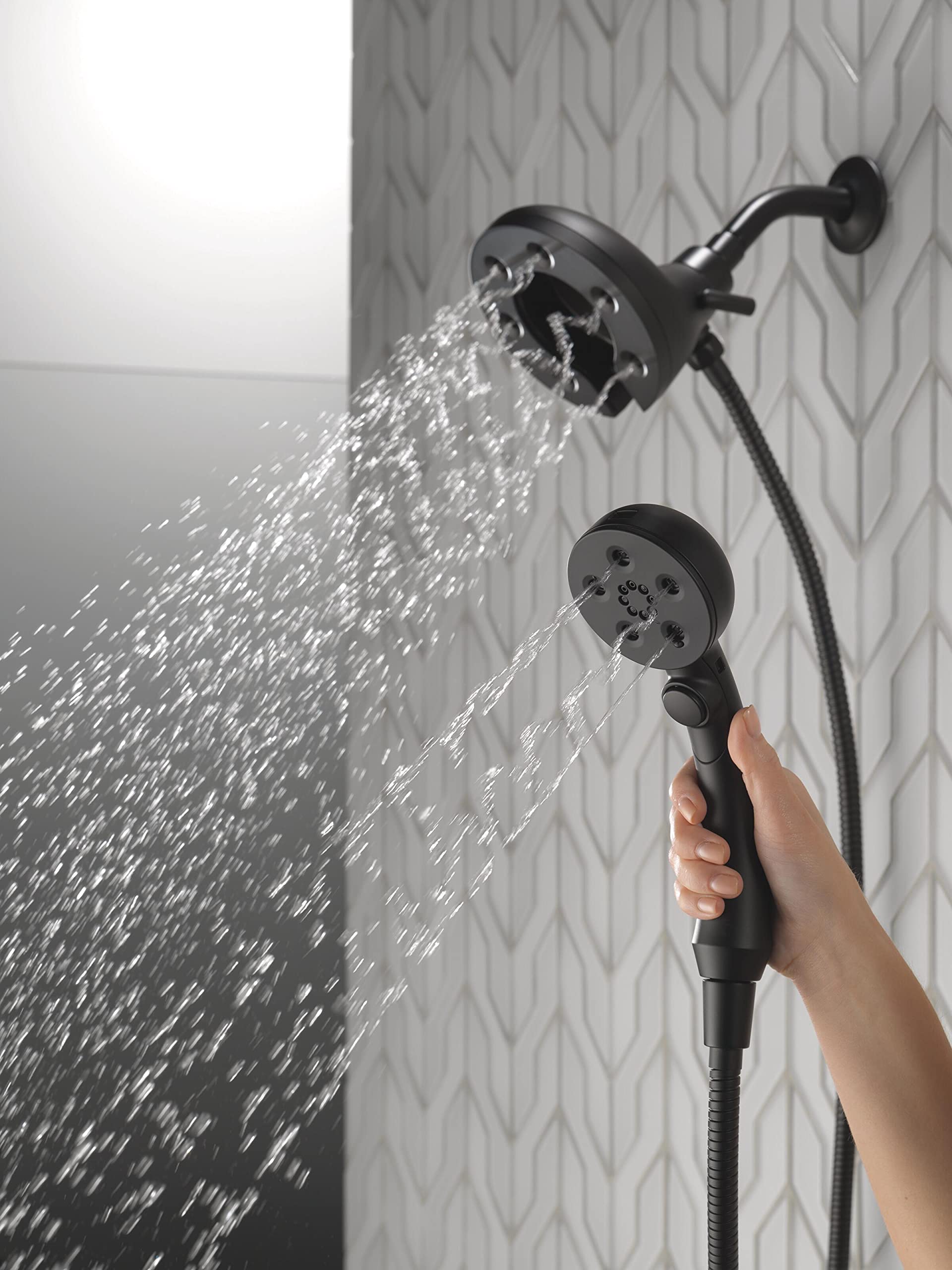 Matte black two-in-one shower system with fixed showerhead and handheld spray head dispensing water simultaneously against te