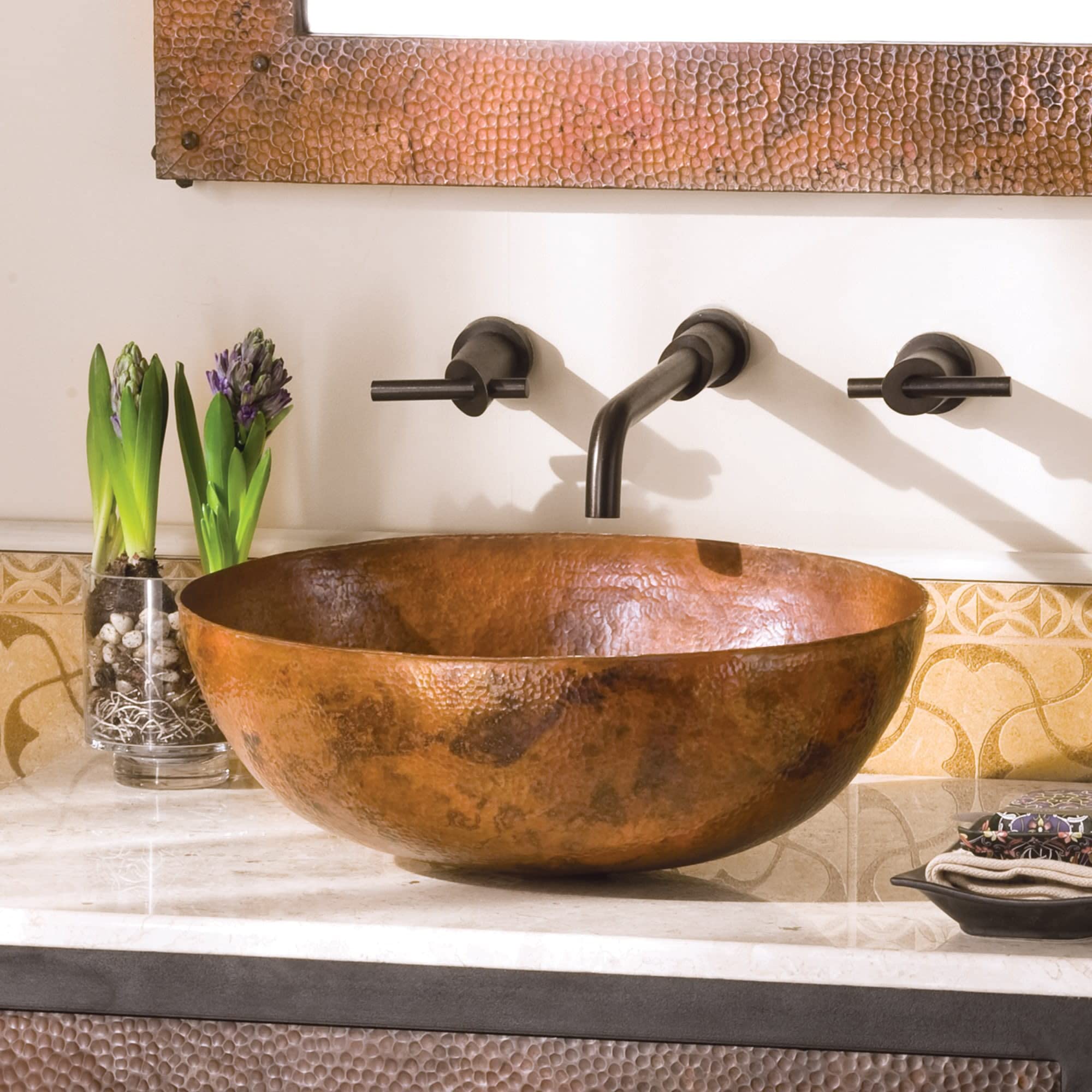 Antique copper oval bathroom sink with hammered texture and oil-rubbed bronze wall-mounted faucet.
