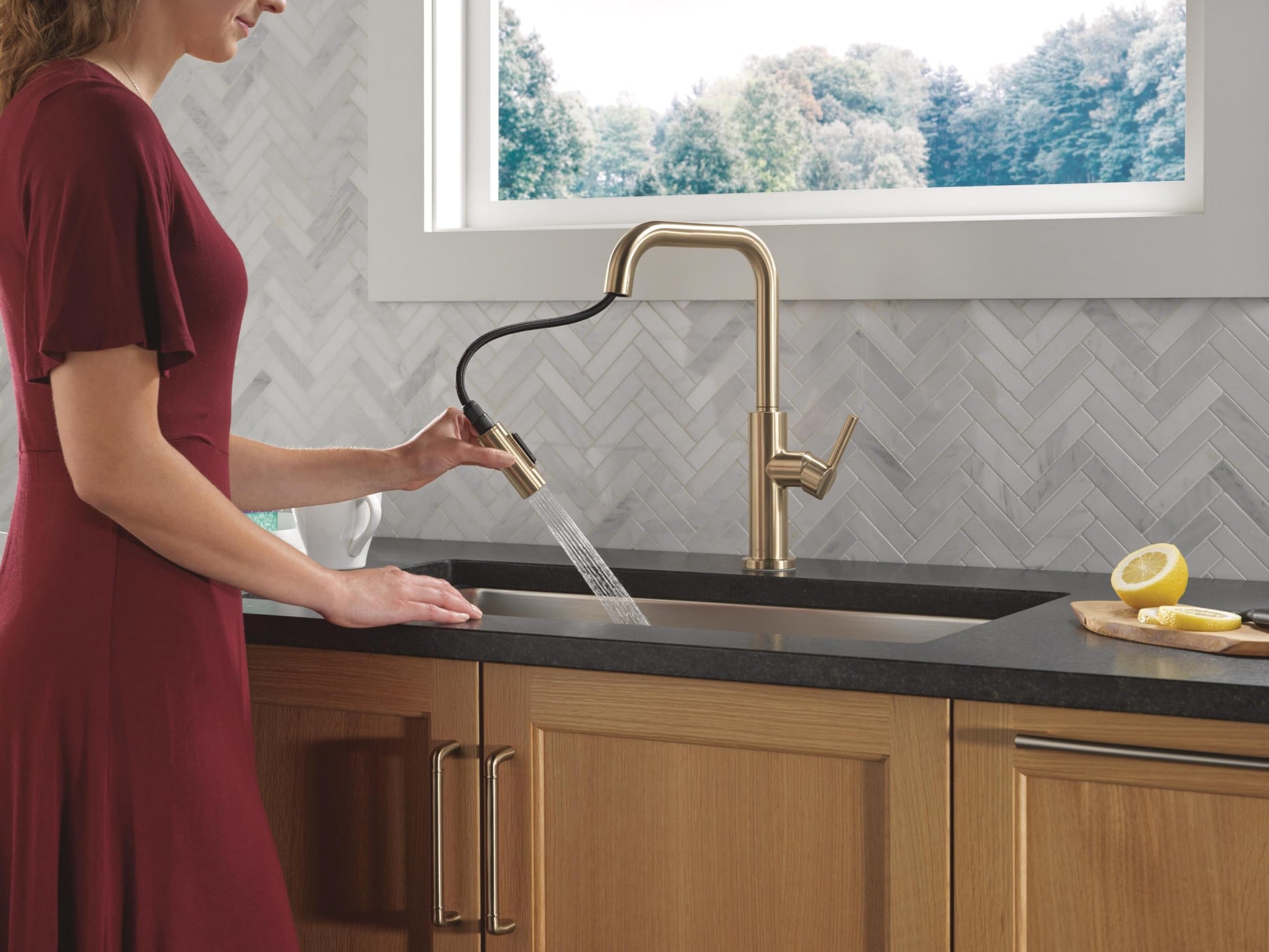 Champagne bronze single-handle pull-down kitchen faucet with curved spout installed over black countertop sink.