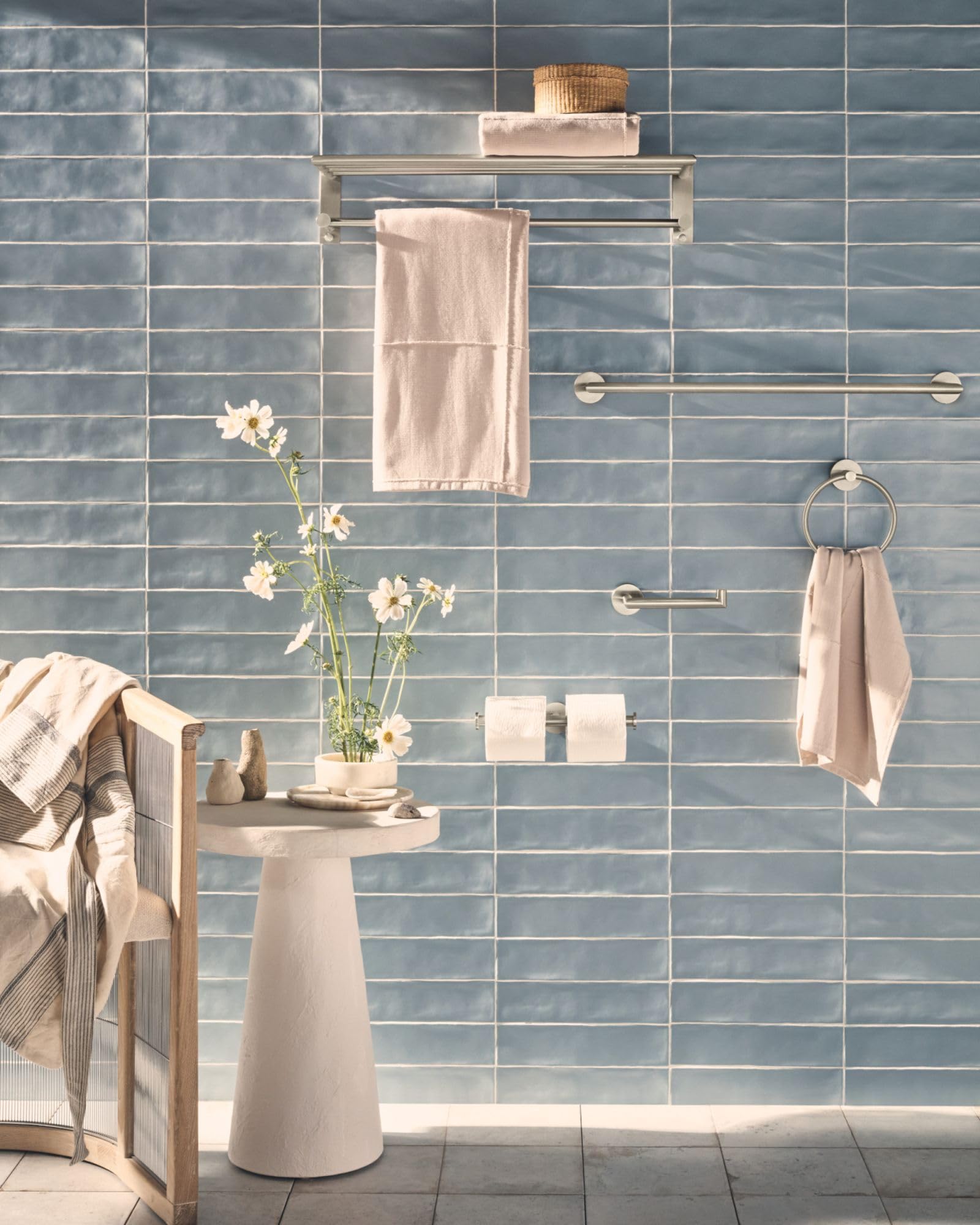 Brushed nickel bathroom shelf with towel bar mounted on blue subway tile wall, displaying folded towels and bath accessories.