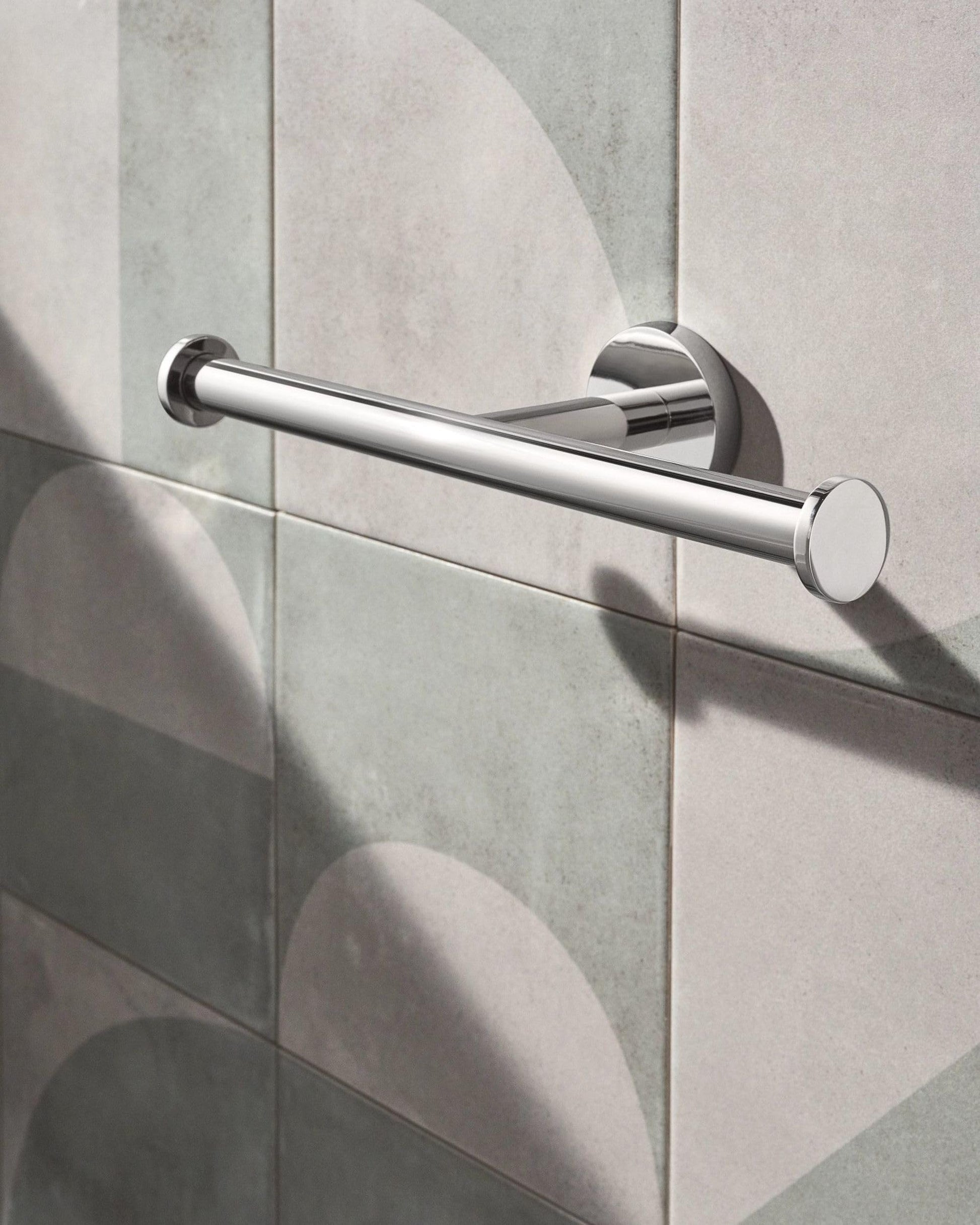 Chrome double toilet paper holder with cylindrical bars mounted horizontally on tiled bathroom wall.
