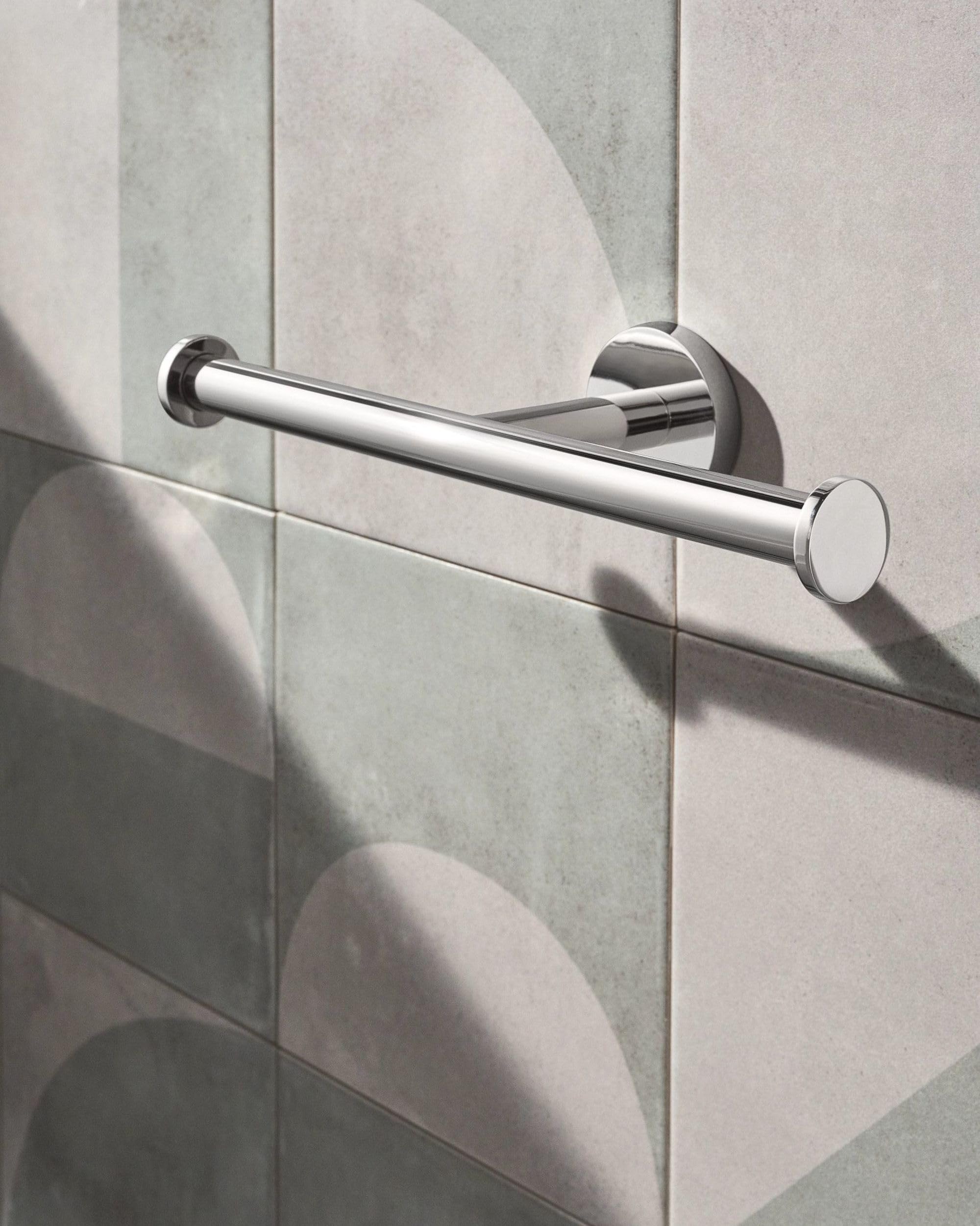 Chrome double toilet paper holder with cylindrical bars mounted horizontally on tiled bathroom wall.