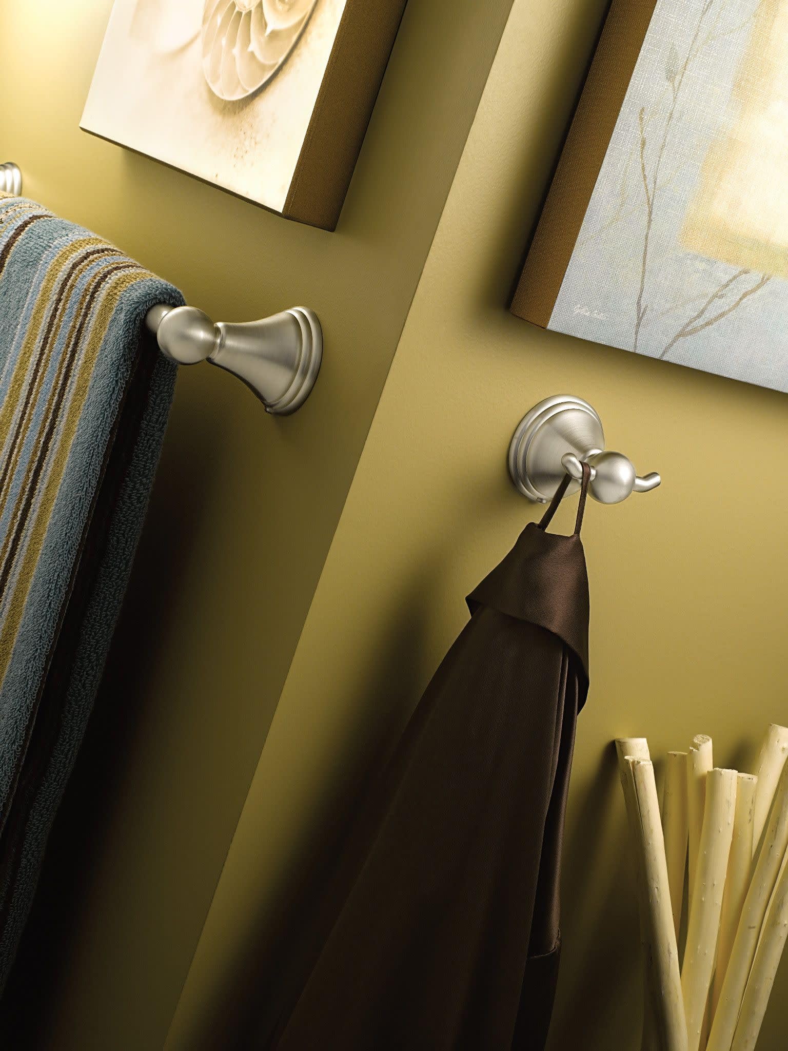 Brushed nickel towel bars mounted on yellow wall with towels draped over them.