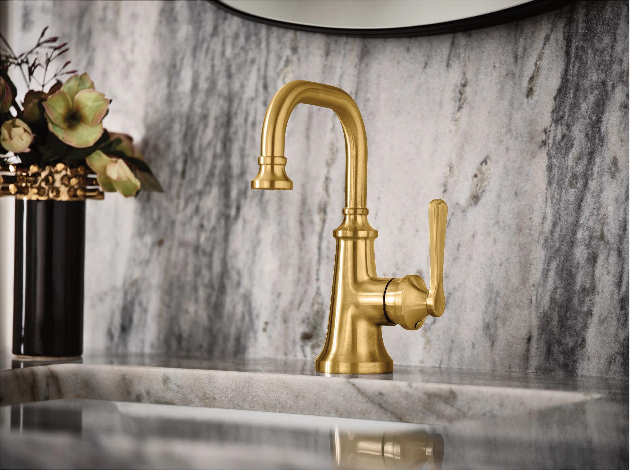 Brushed gold single-handle bathroom sink faucet with curved spout and traditional lever handle on marble countertop.