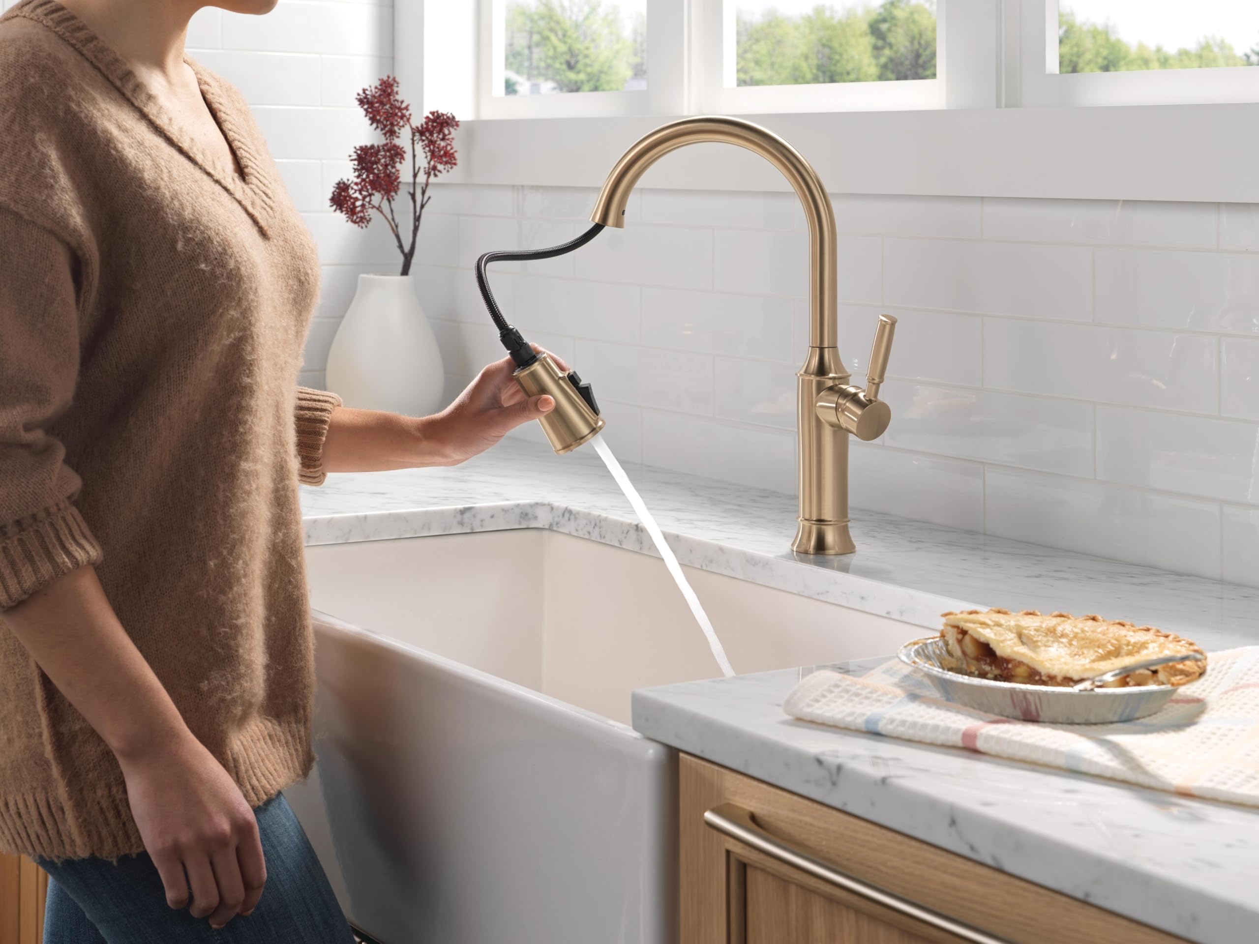 Champagne bronze single-handle pull-down kitchen faucet with spray nozzle extended over white farmhouse sink.