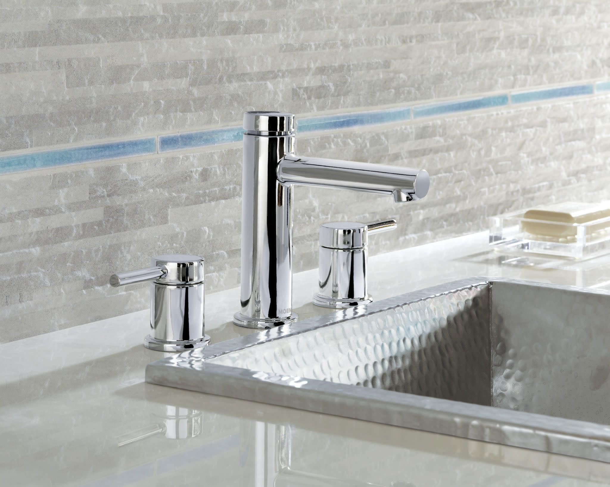 Chrome two-handle bathroom faucet with cylindrical handles and curved spout mounted on white sink counter.