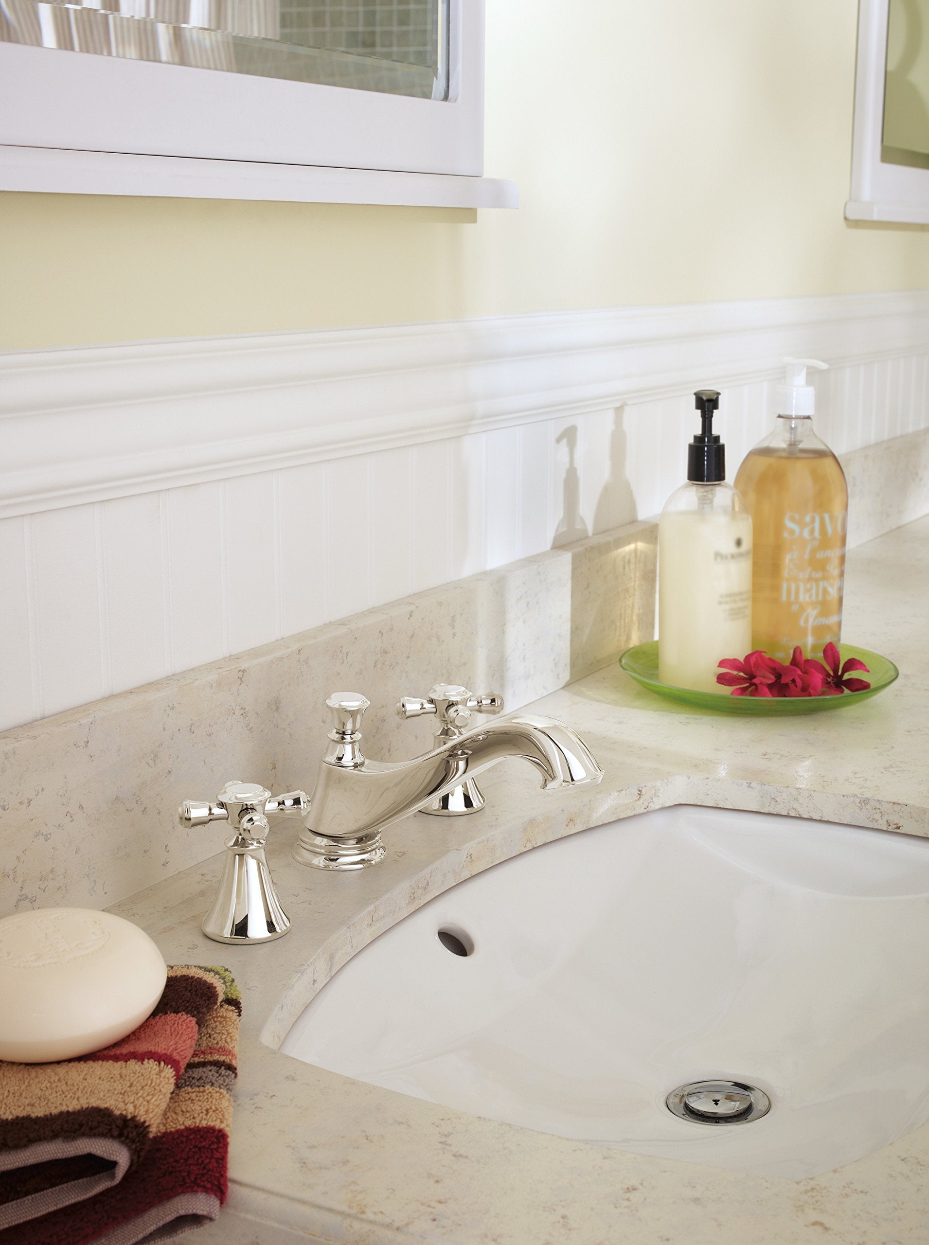 Polished nickel deck mount faucet with cross handles and curved spout installed on marble bathroom vanity.