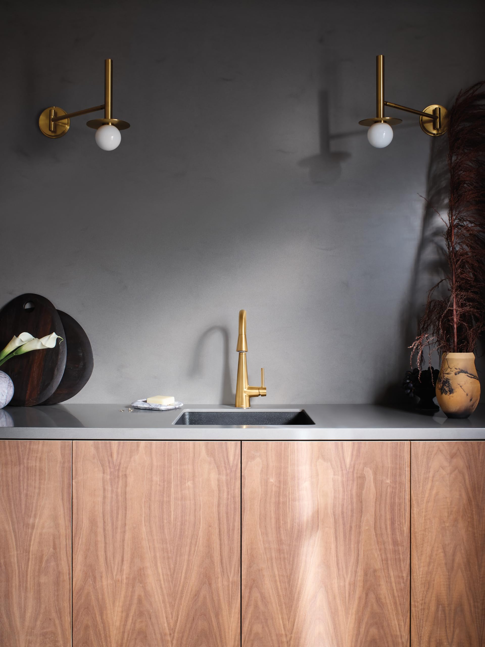 Brushed gold single-handle high-arc pulldown faucet mounted above a modern kitchen sink with gray countertop.