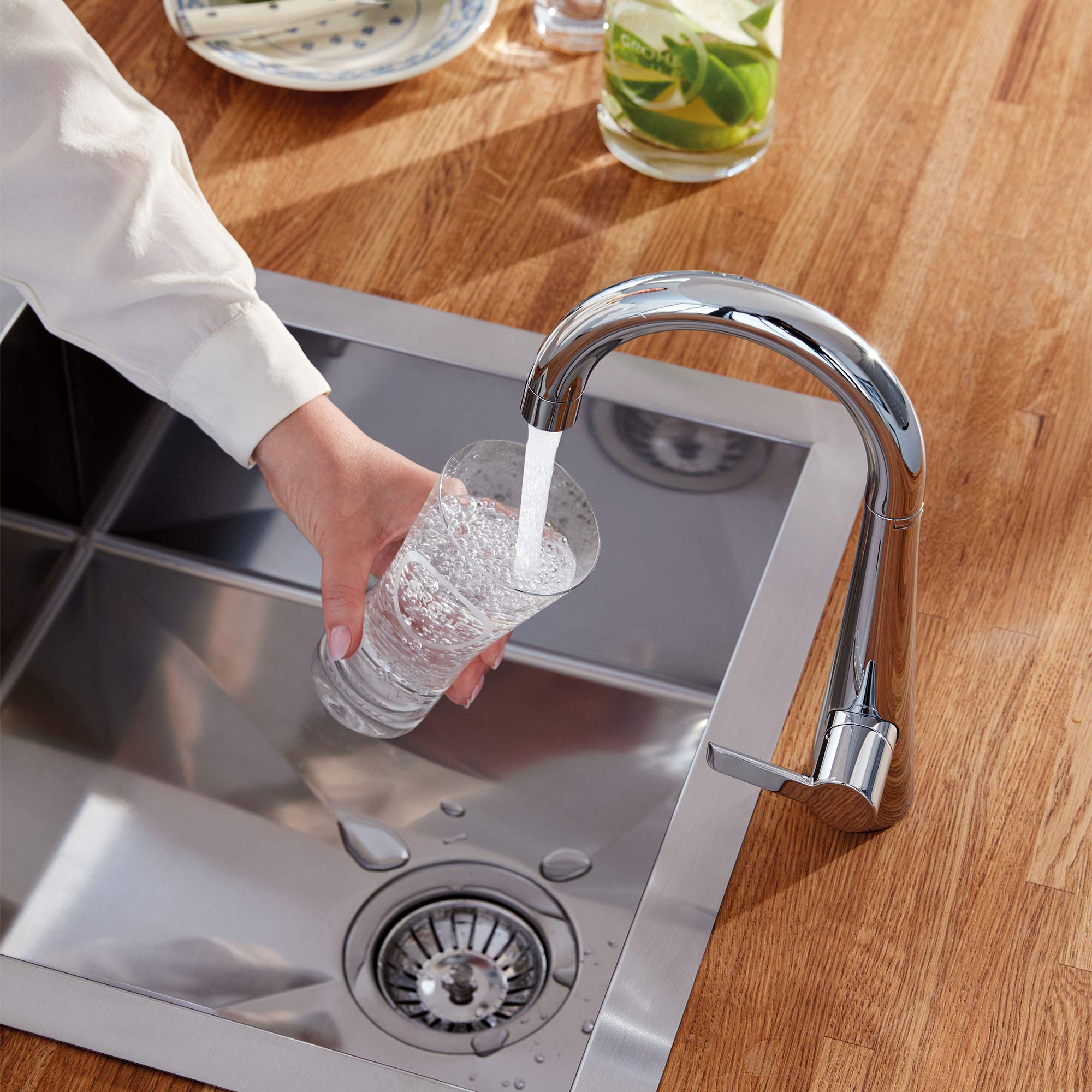 Chrome single-handle beverage faucet with curved spout dispensing filtered water into a glass over a stainless steel sink.
