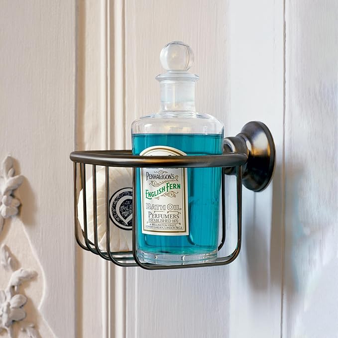 Chrome shower basket with rectangular wire frame holding a glass bottle of blue liquid, mounted on white wall tile.