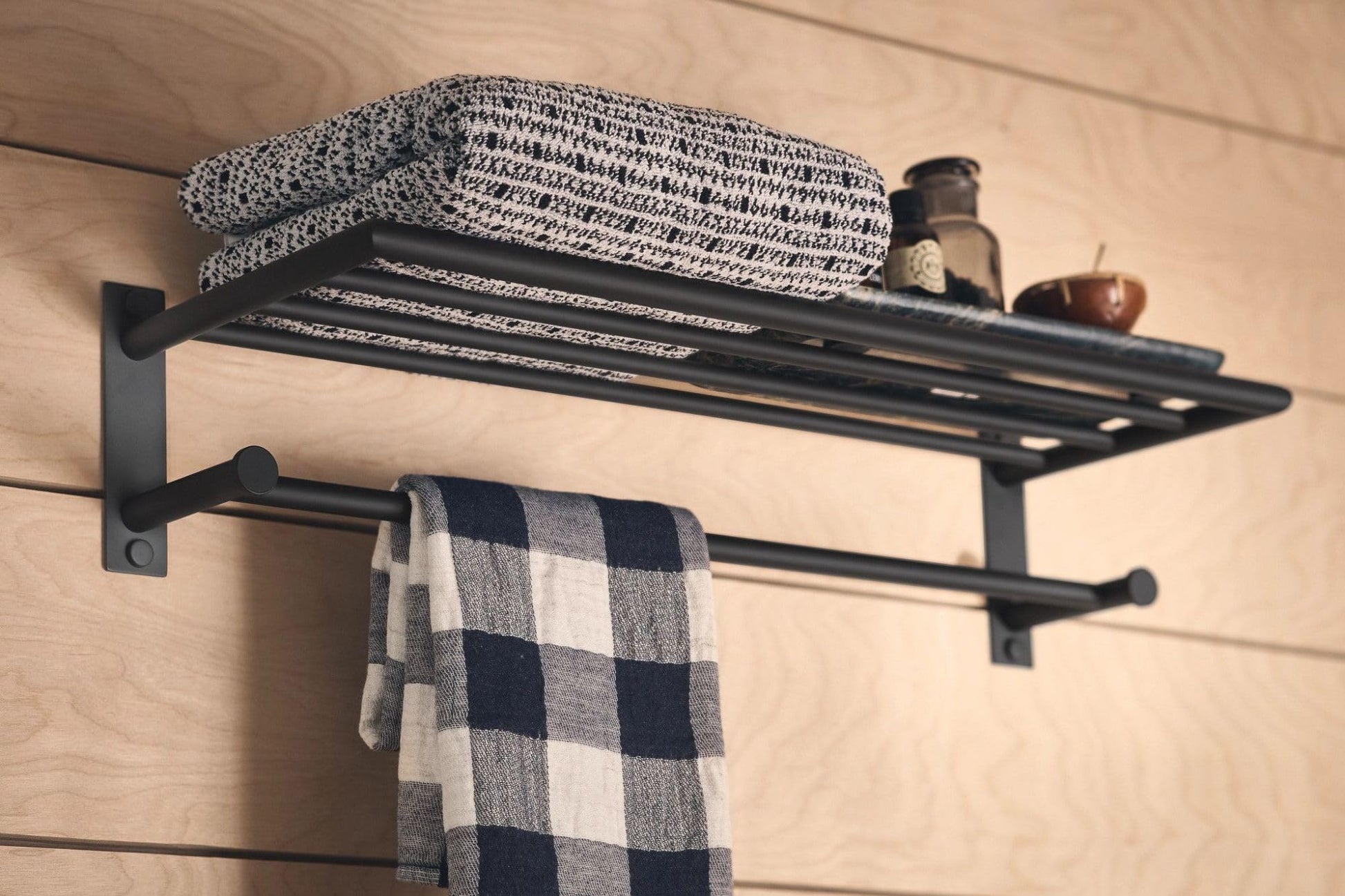 Matte black wall-mounted shelf with towel bar holding folded towels and bath accessories.