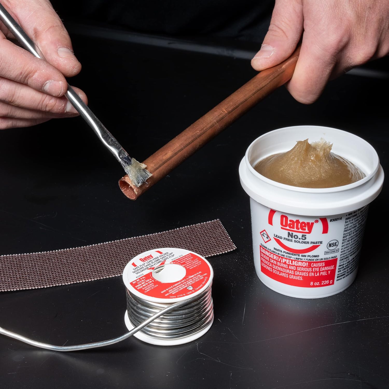 Oatey No. 5 paste flux in white container with red label displayed alongside solder and soldering tools.
