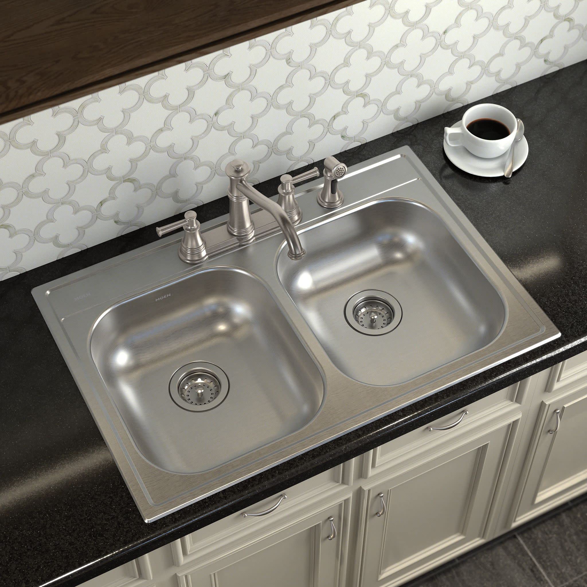 Stainless steel two-handle high arc kitchen faucet with side spray mounted on double basin sink with dark countertop.
