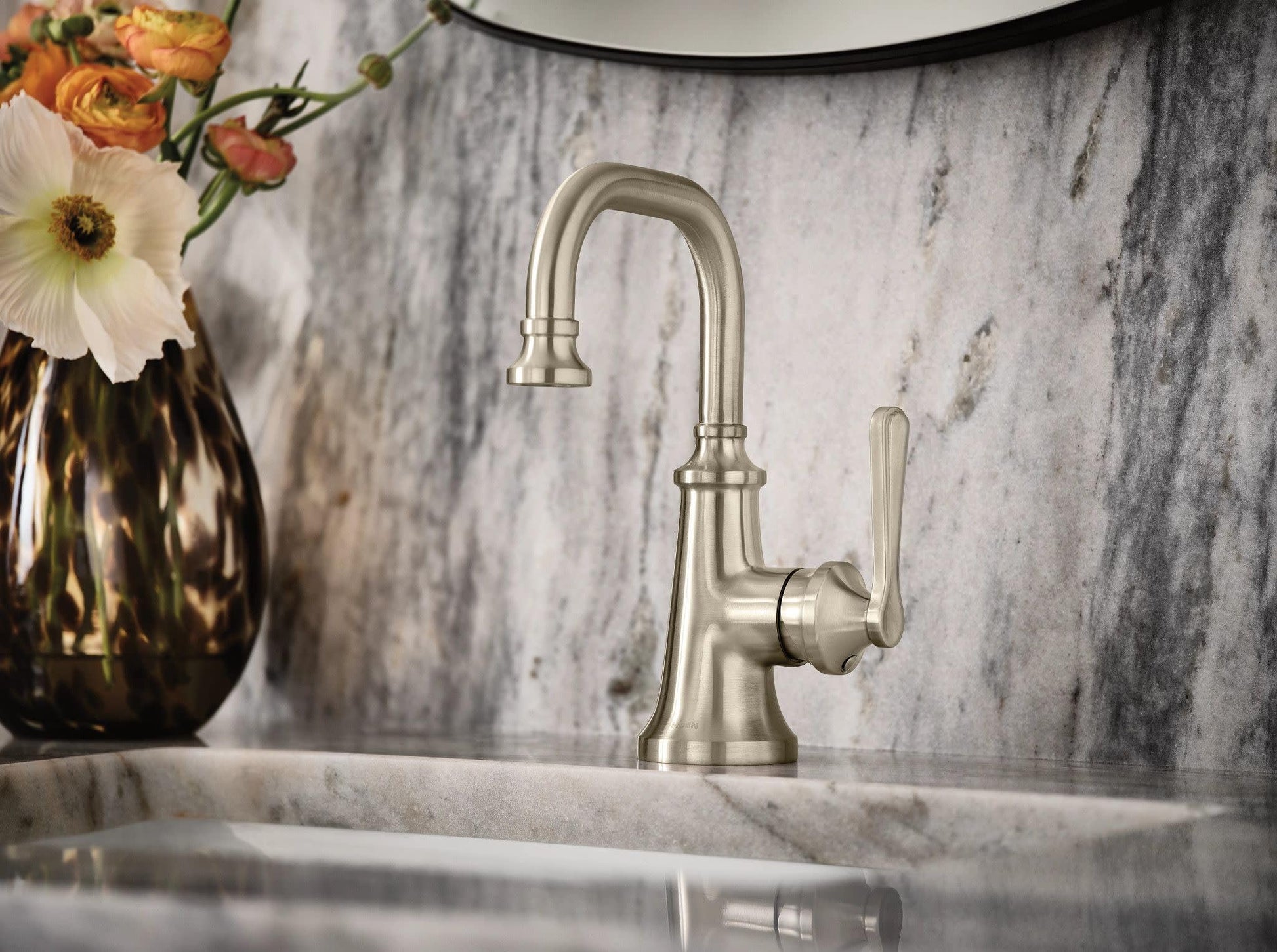 Brushed nickel single-handle bathroom faucet with curved spout and lever handle on marble sink countertop.