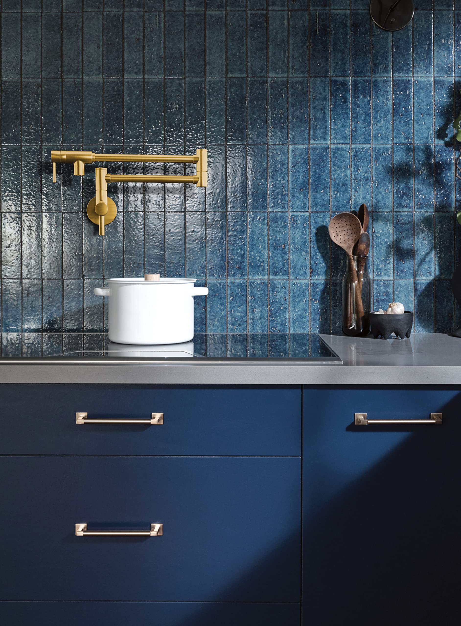 Brushed gold wall-mounted pot filler faucet with double-jointed folding swing arm above stovetop.