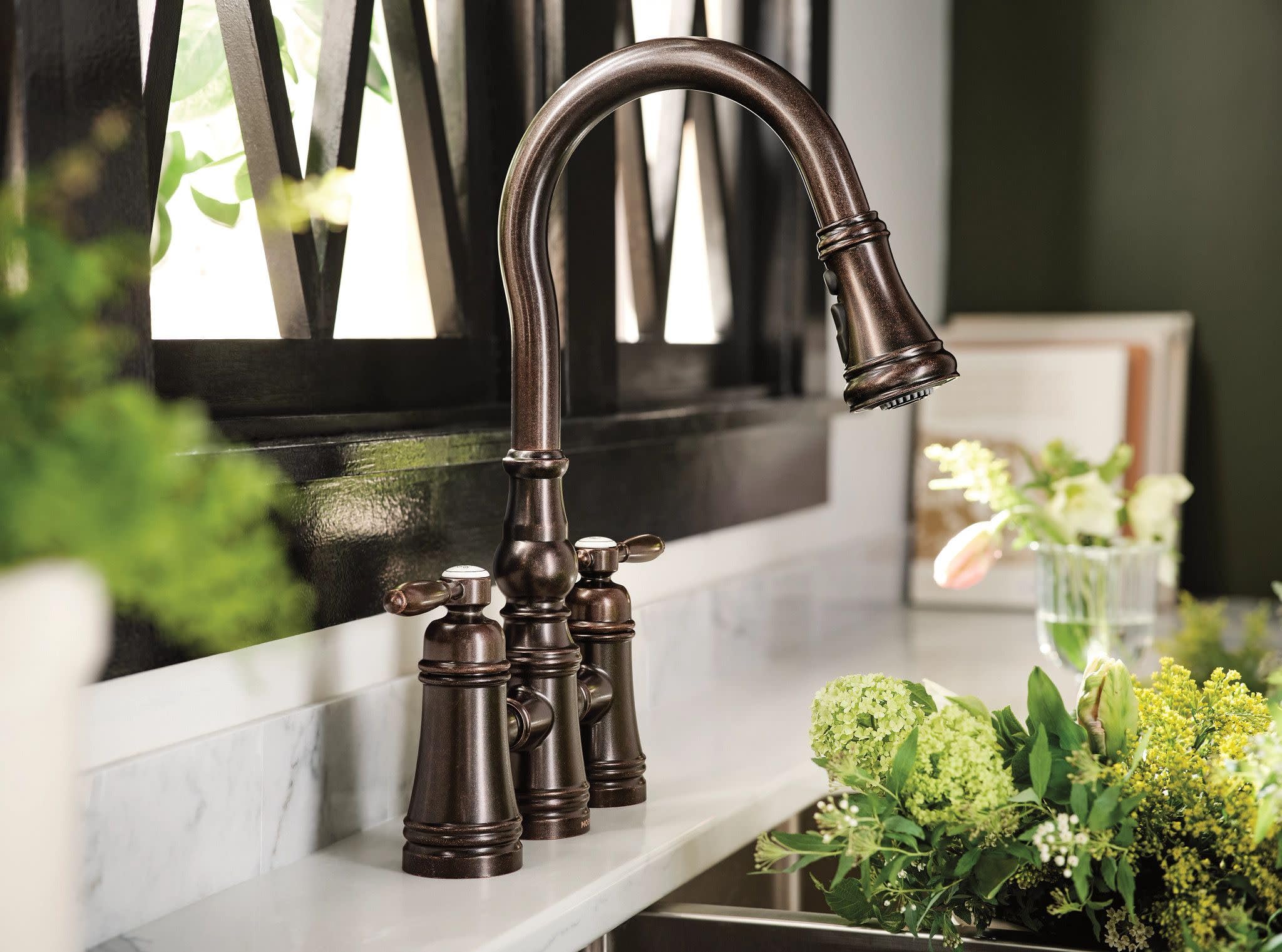 Oil rubbed bronze bridge kitchen faucet with two handles and pulldown spout over white countertop.