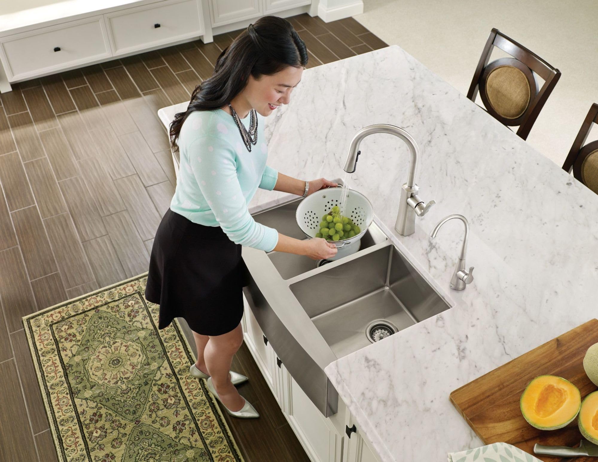 Stainless steel transitional cold water kitchen faucet with curved spout installed above marble countertop sink.