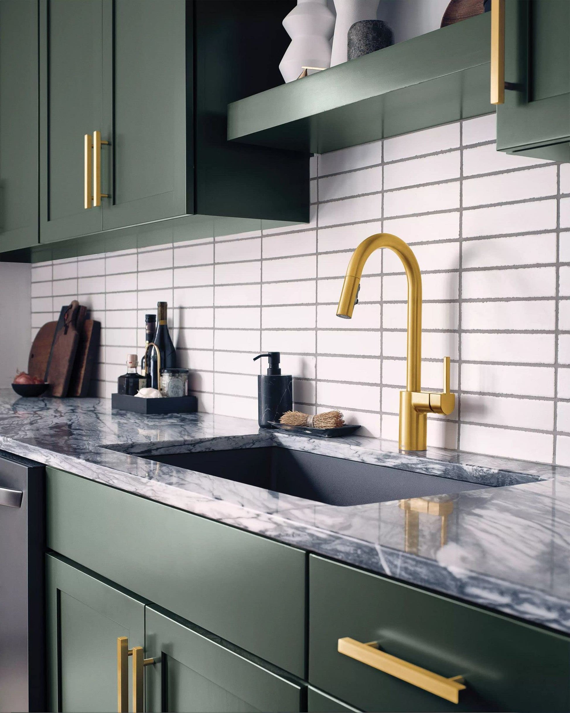 Brushed gold pulldown kitchen faucet with single handle mounted above a sink with marble countertop and white subway tile bac
