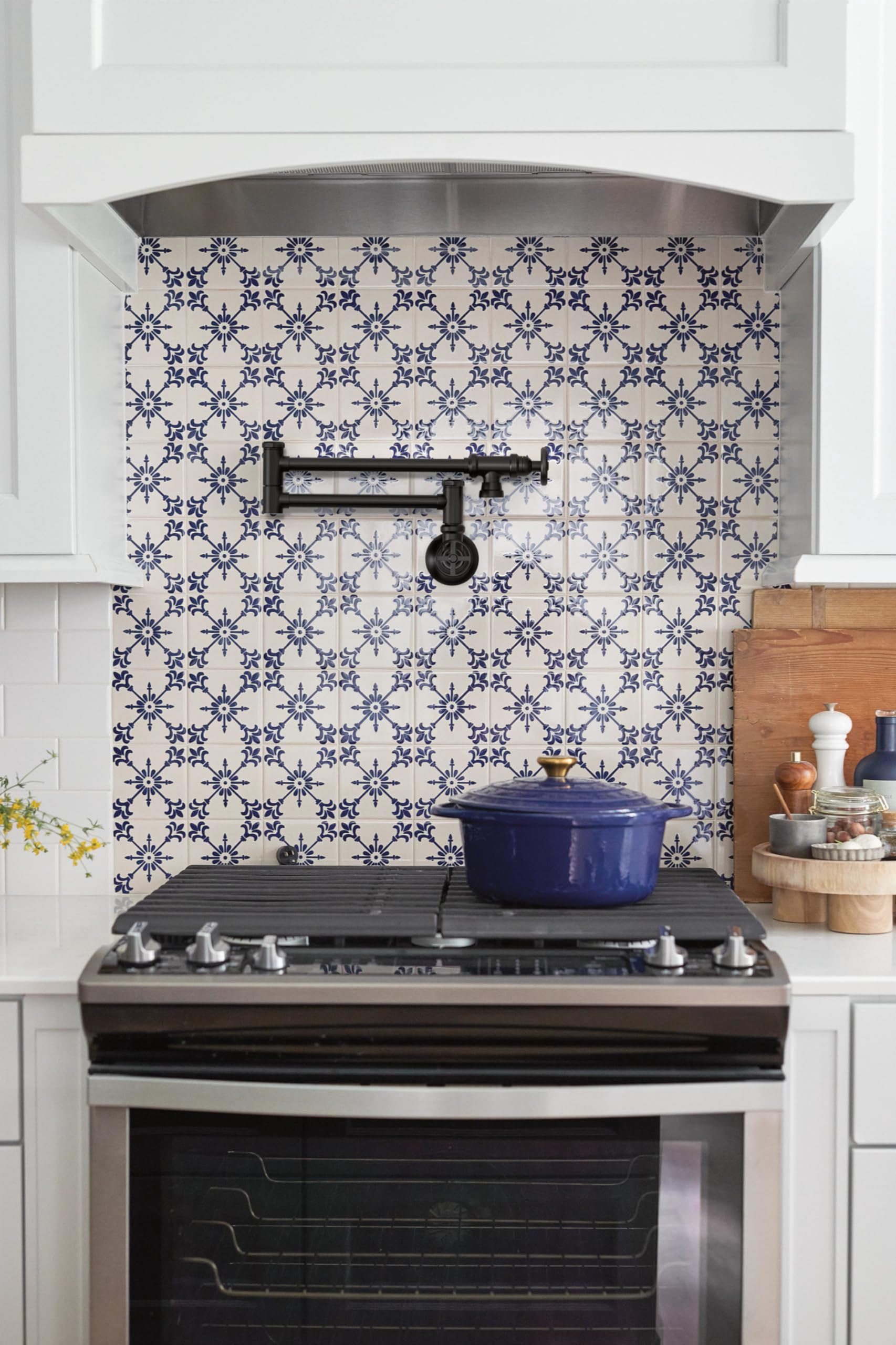 Matte black wall-mounted pot filler faucet with folding swing arm above kitchen stove.