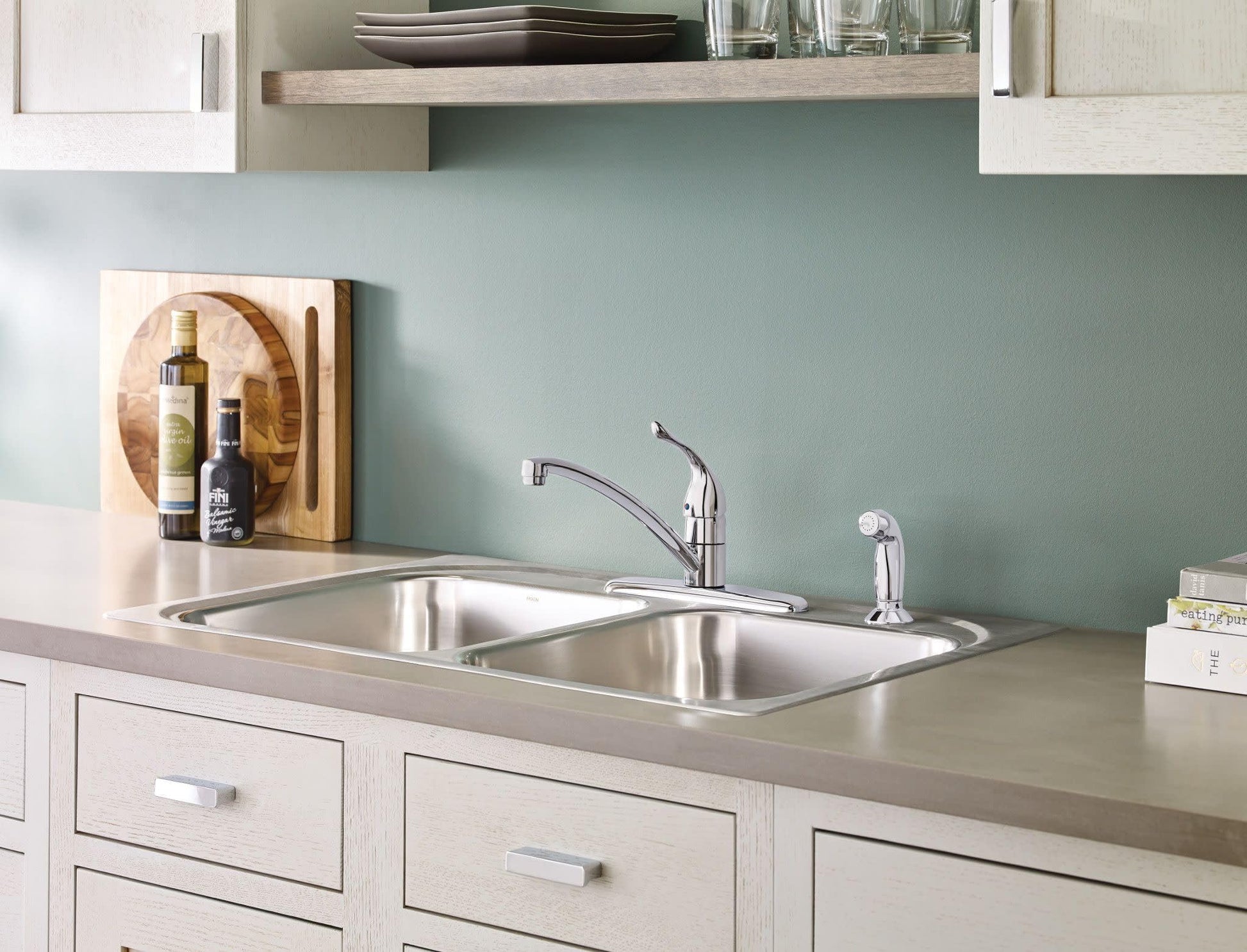 Chrome single-handle kitchen faucet with curved spout mounted on double basin stainless steel sink.