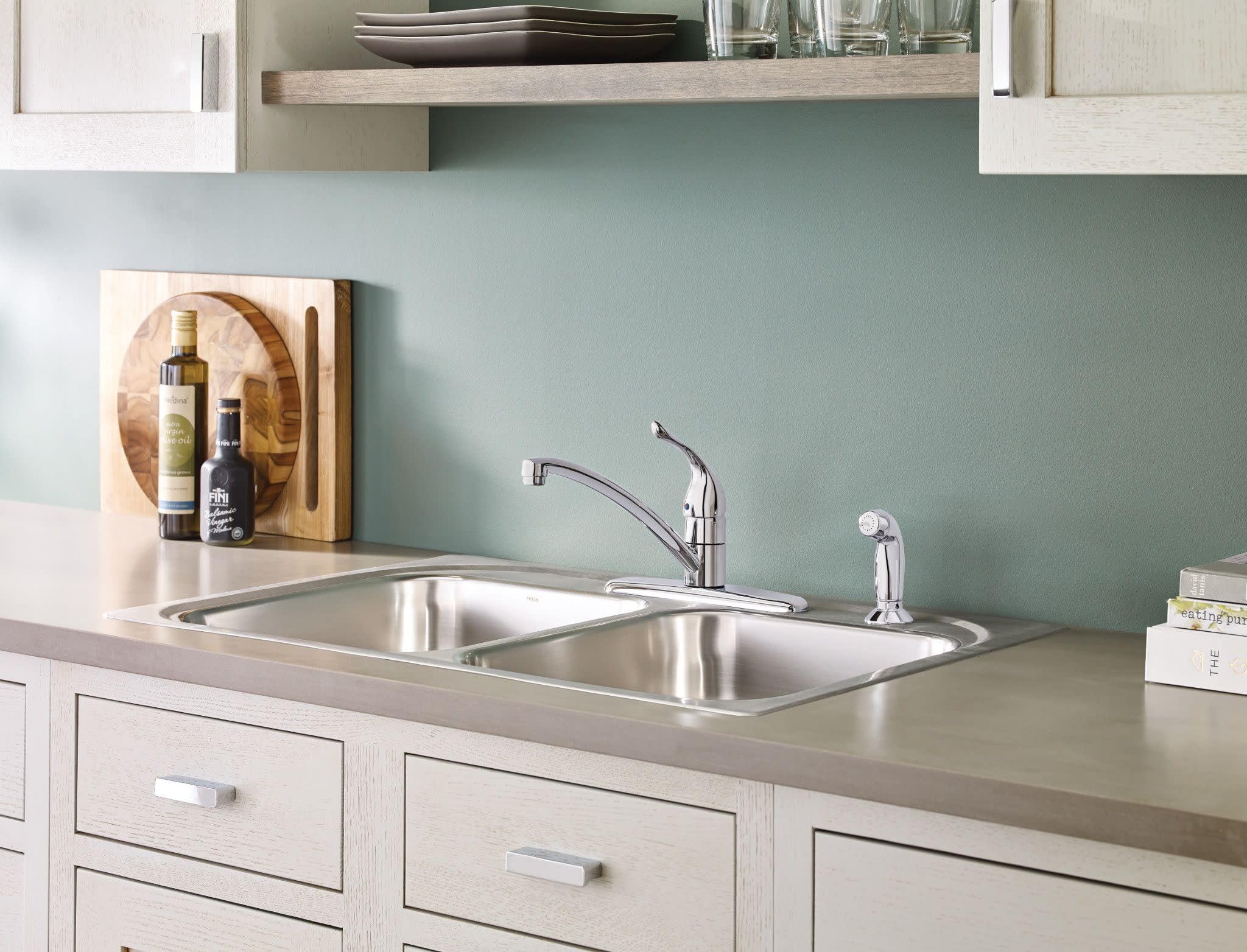 Chrome single-handle kitchen faucet with curved spout mounted on double basin stainless steel sink.