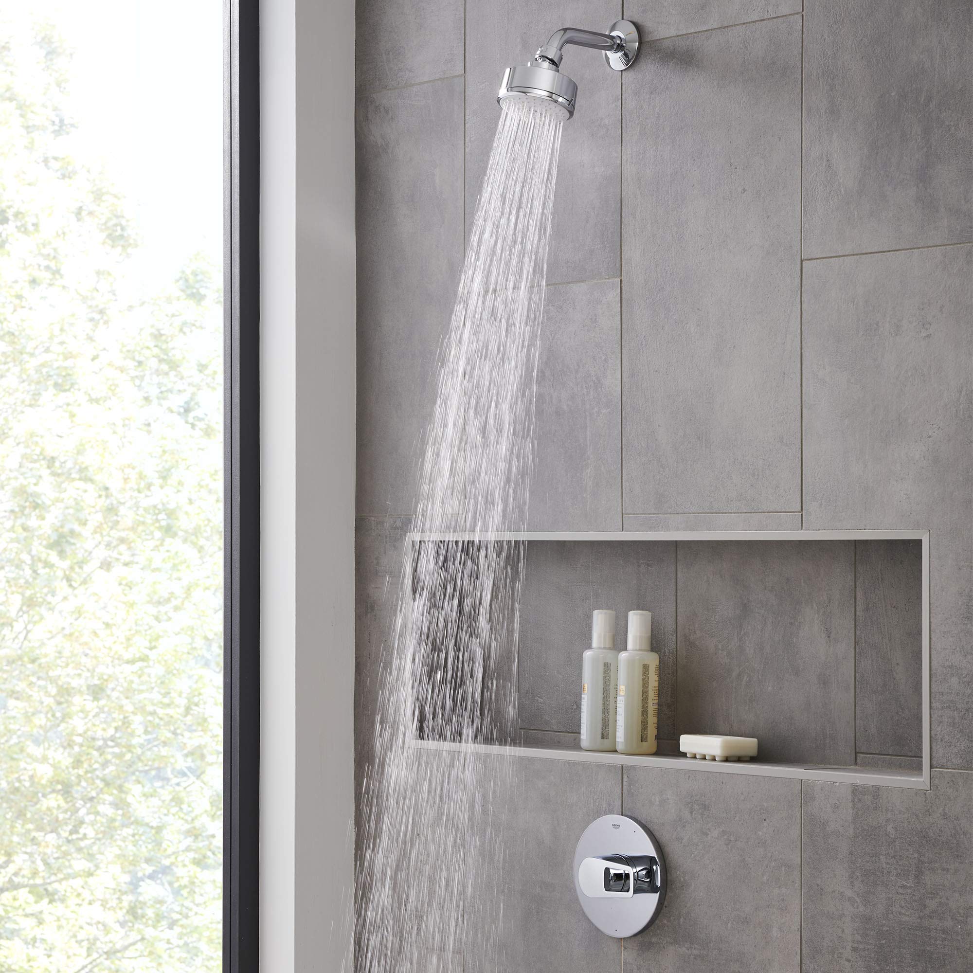 Chrome pressure balance valve trim with round handle and overhead rainfall showerhead mounted on gray tile wall.