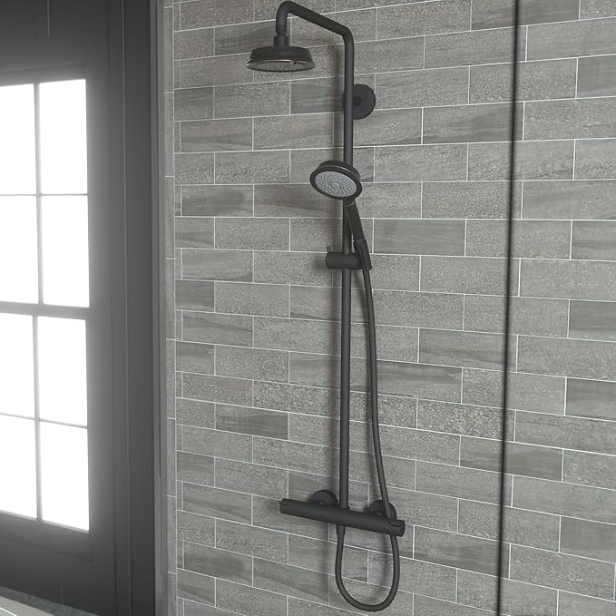 Rubbed bronze shower system mounted on gray tile wall with overhead showerhead, hand shower, and control valve.
