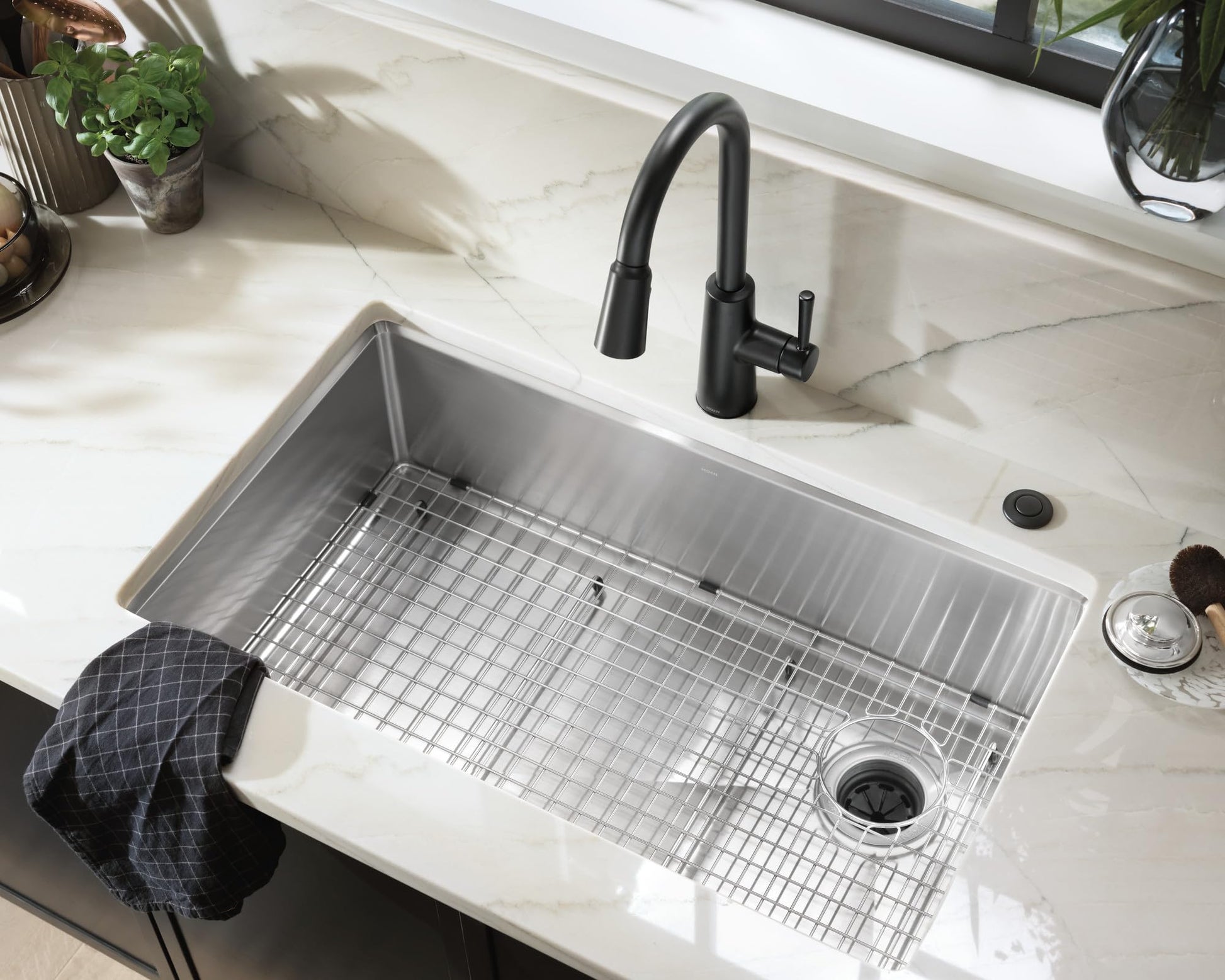 Matte black circular air switch button mounted on white marble countertop next to kitchen sink.