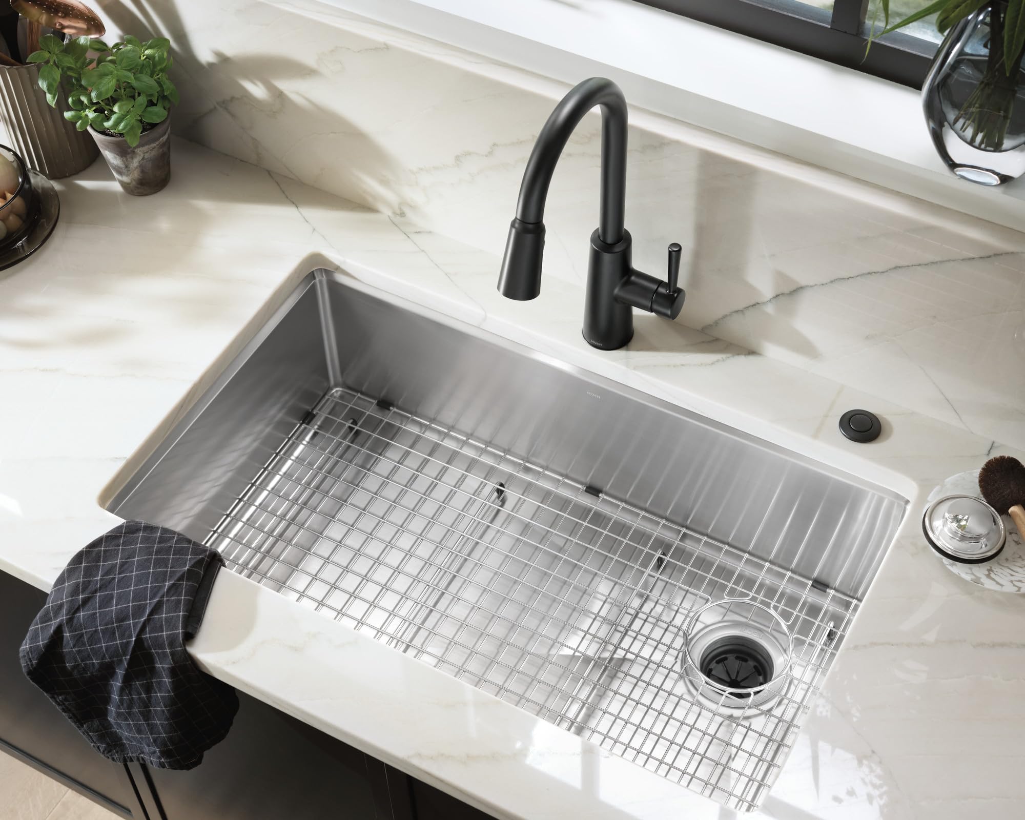 Matte black circular air switch button mounted on white marble countertop next to kitchen sink.