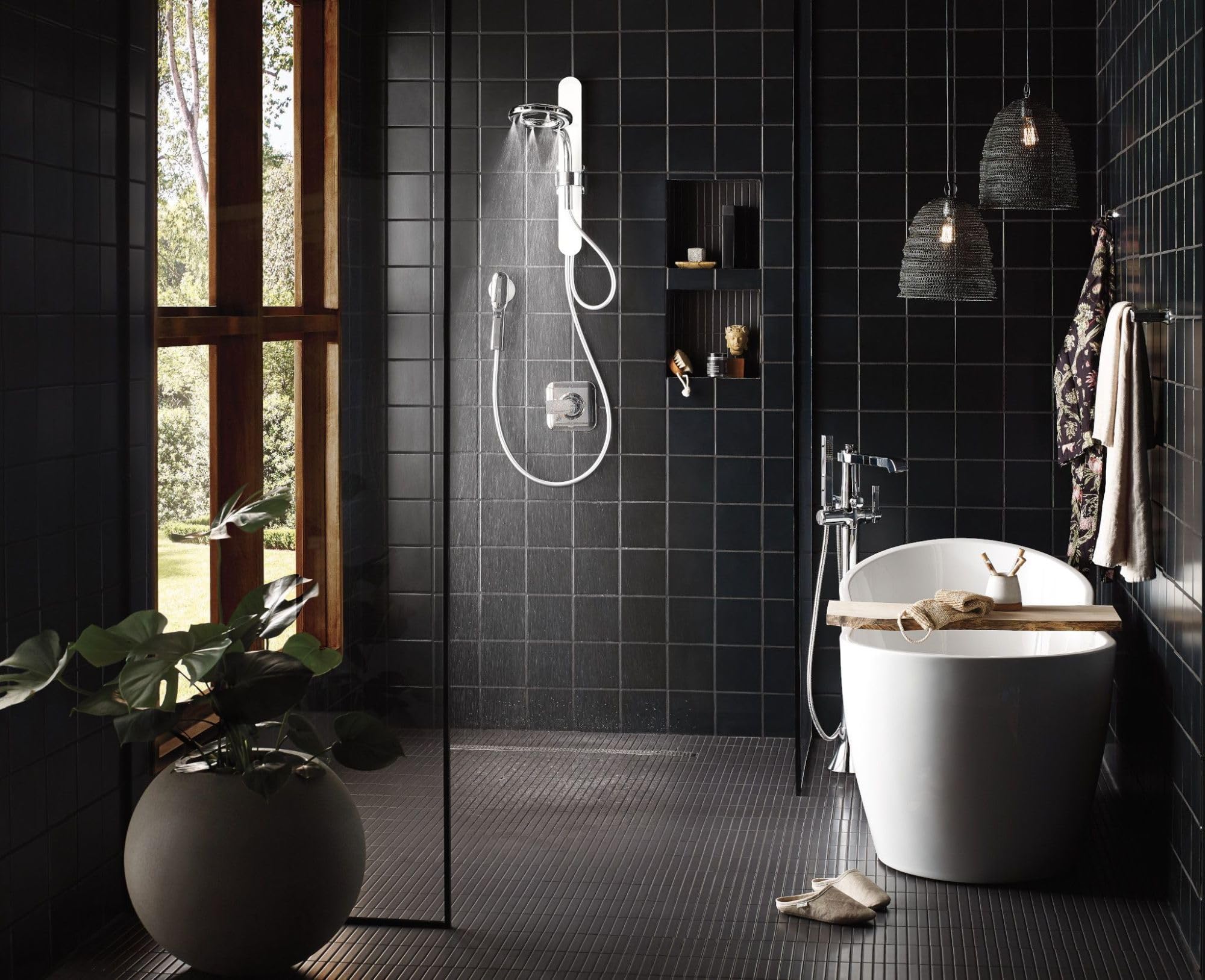 Chrome floor-mounted tub filler with single handle and handheld showerhead spraying water into white soaking tub.