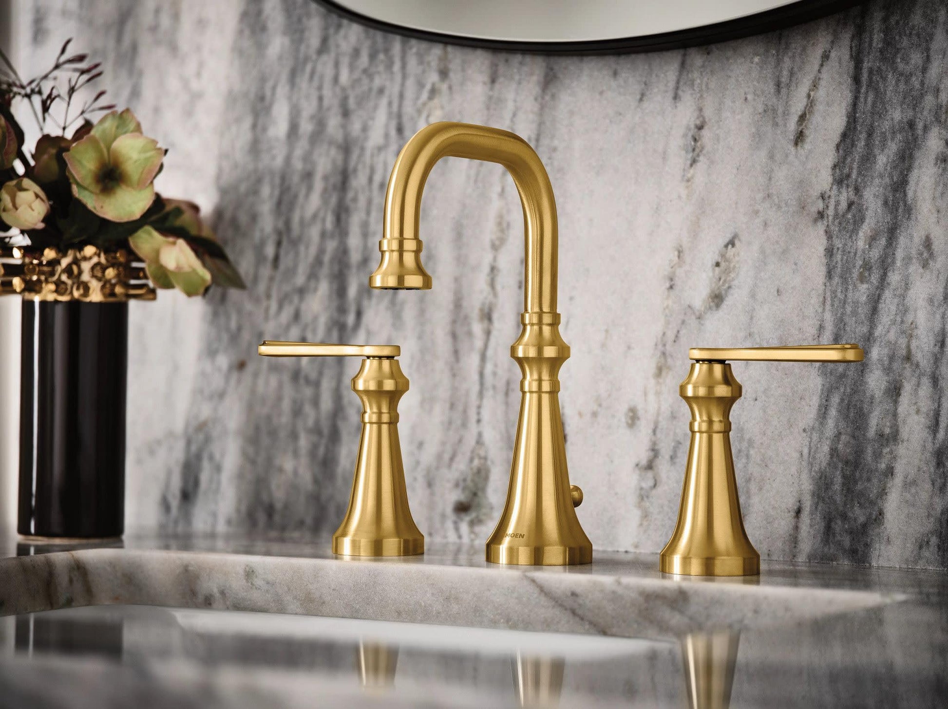 Brushed gold two-handle bathroom faucet with curved center spout and tapered base handles on marble countertop.